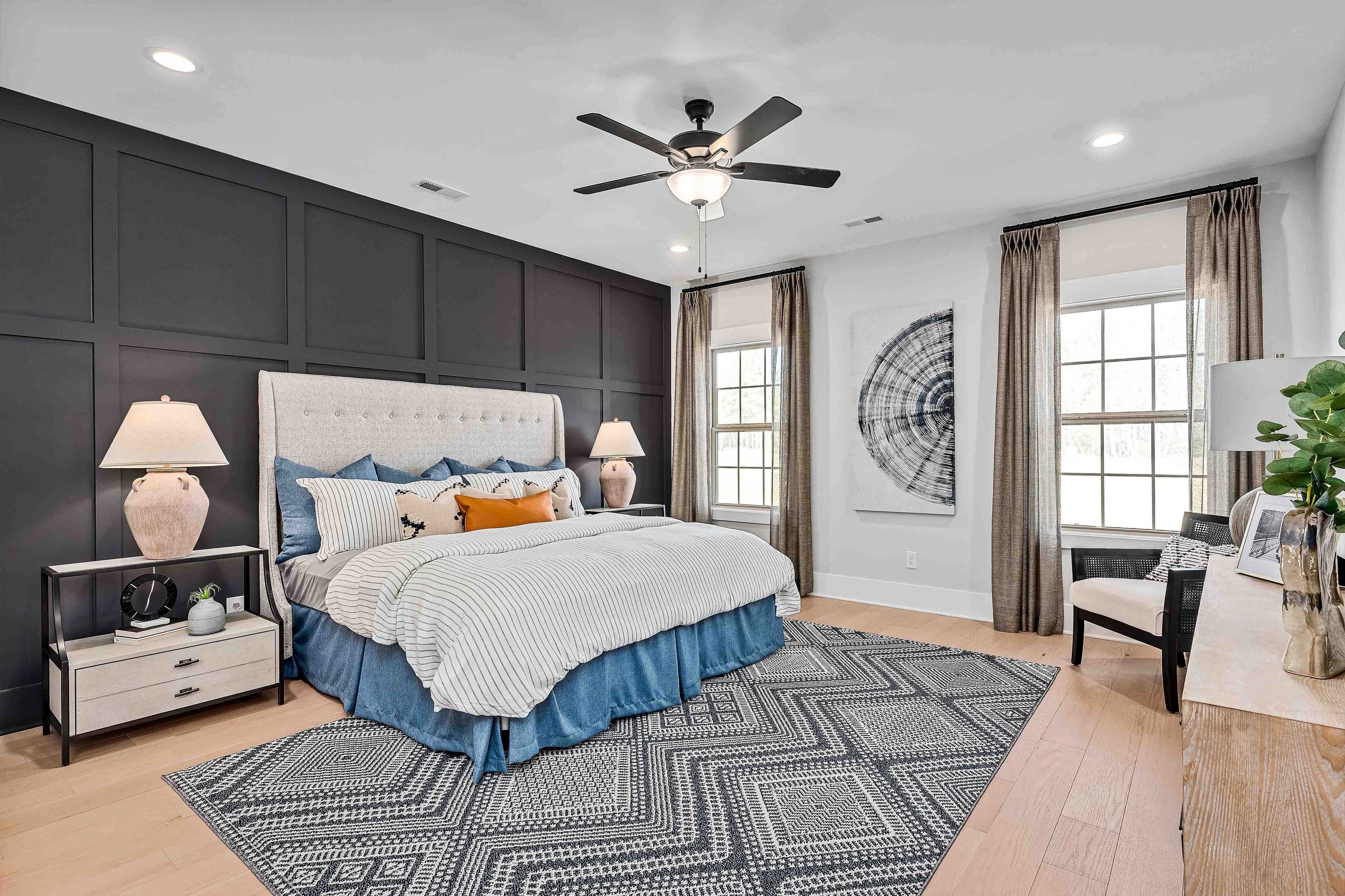 Elegant primary bedroom at Cain Park in Hartselle Alabama with black accent wall tufted king bed ceiling fan and hardwood floors