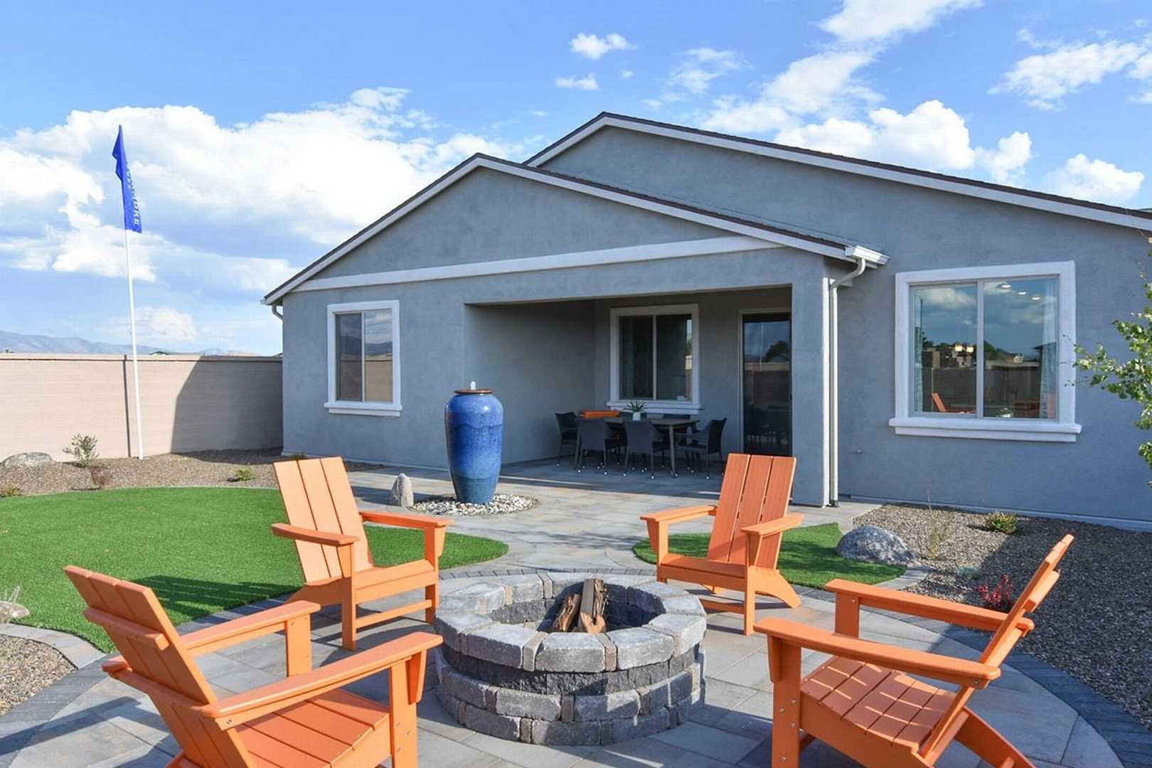 Cozy backyard patio with stone fire pit, orange Adirondack chairs, and covered seating at North Ridge Pronghorn Ranch in Prescott Valley AZ by Davidson Homes