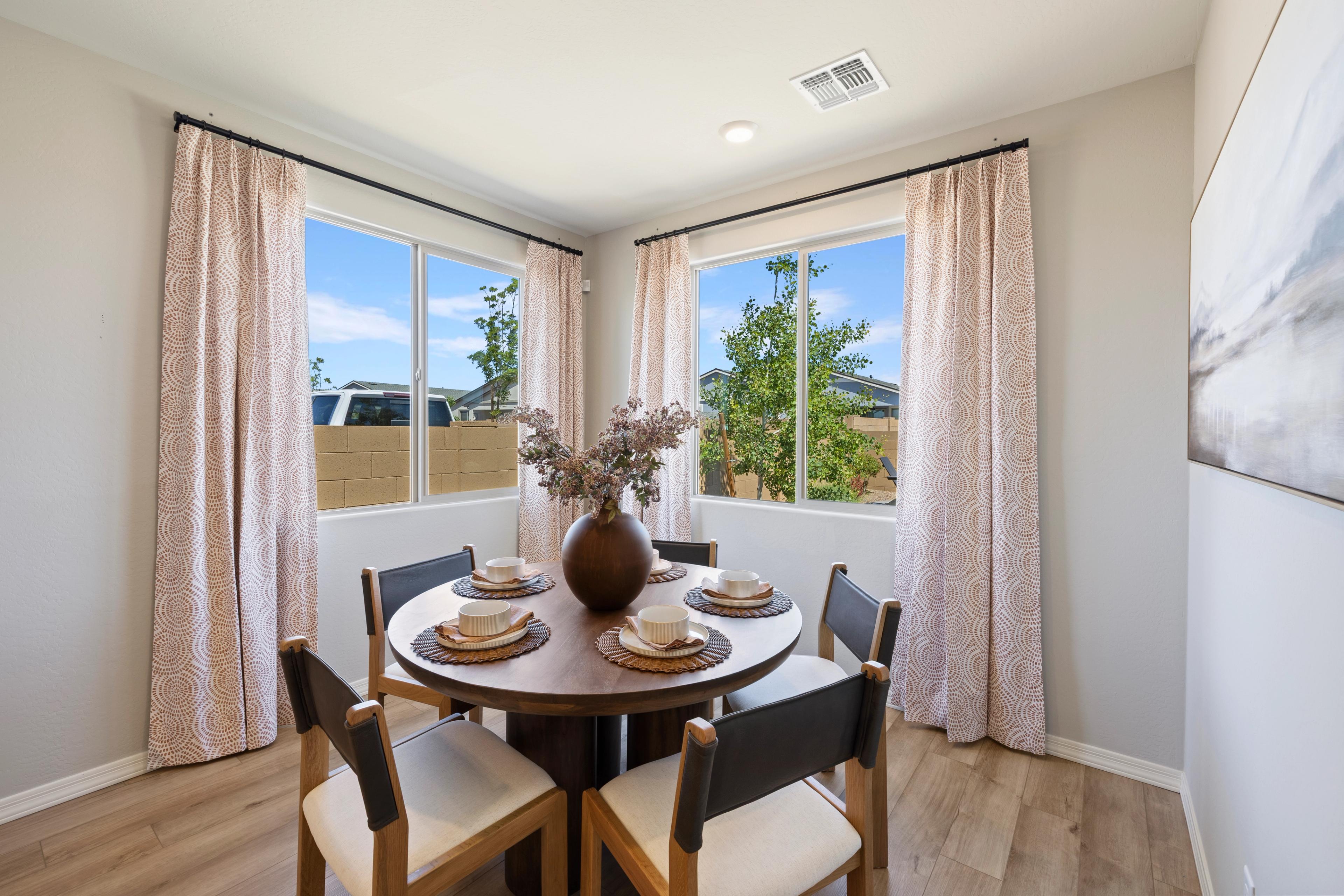 Spacious dining room with round wood table, set plates, and large windows overlooking trees at North Ridge, Pronghorn Ranch in Prescott Valley AZ