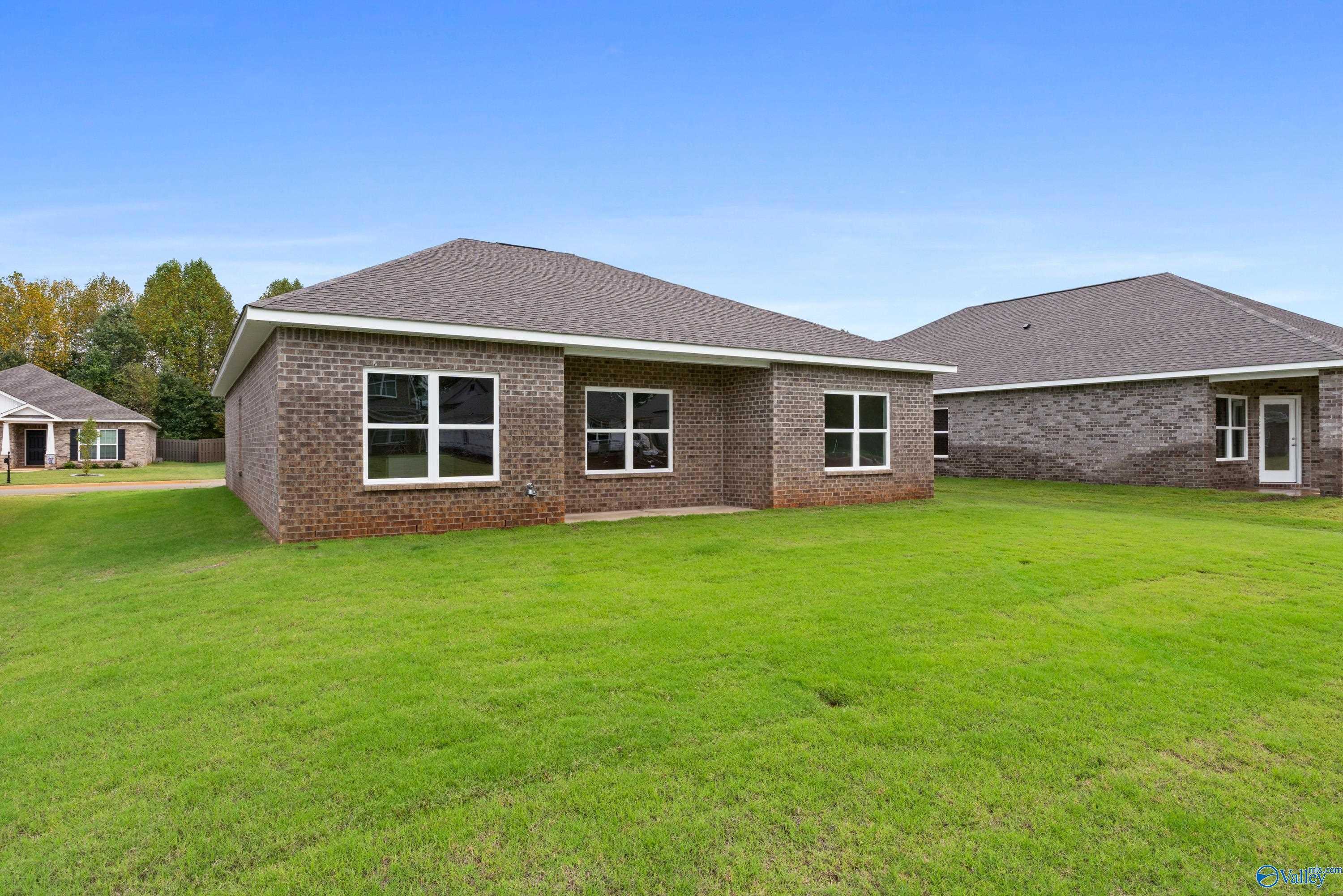 Brick single-story home with large windows, expansive green yard, and neighboring houses in Ricketts Farm, Athens, Alabama - Davidson Homes The Asheville C