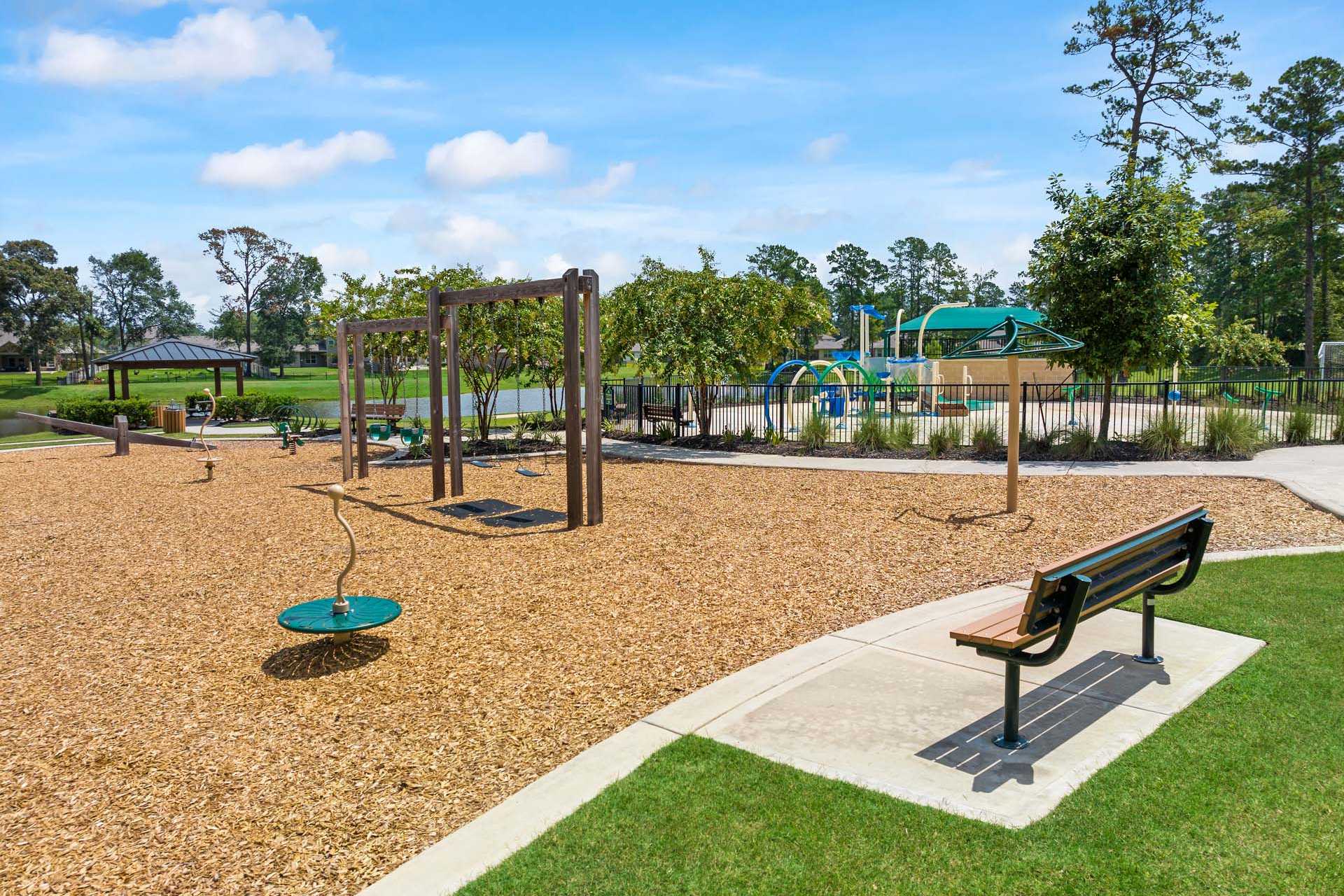 Children's playground at Lakes at Black Oak in Magnolia Texas with swings, green slide, wooden climbers and shaded benches