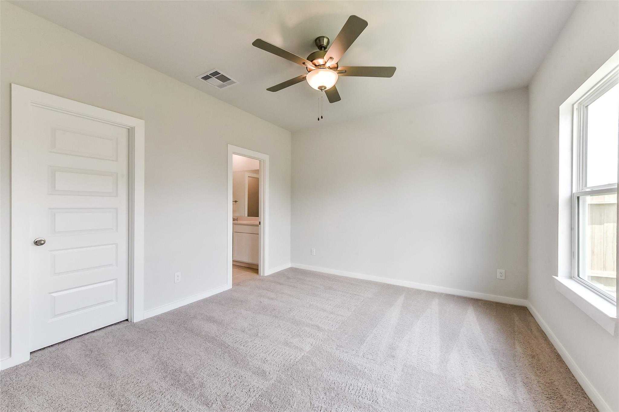 Spacious secondary bedroom with beige carpet, ceiling fan, and en-suite bath in Davidson Homes The Frio F, Dayton, Texas