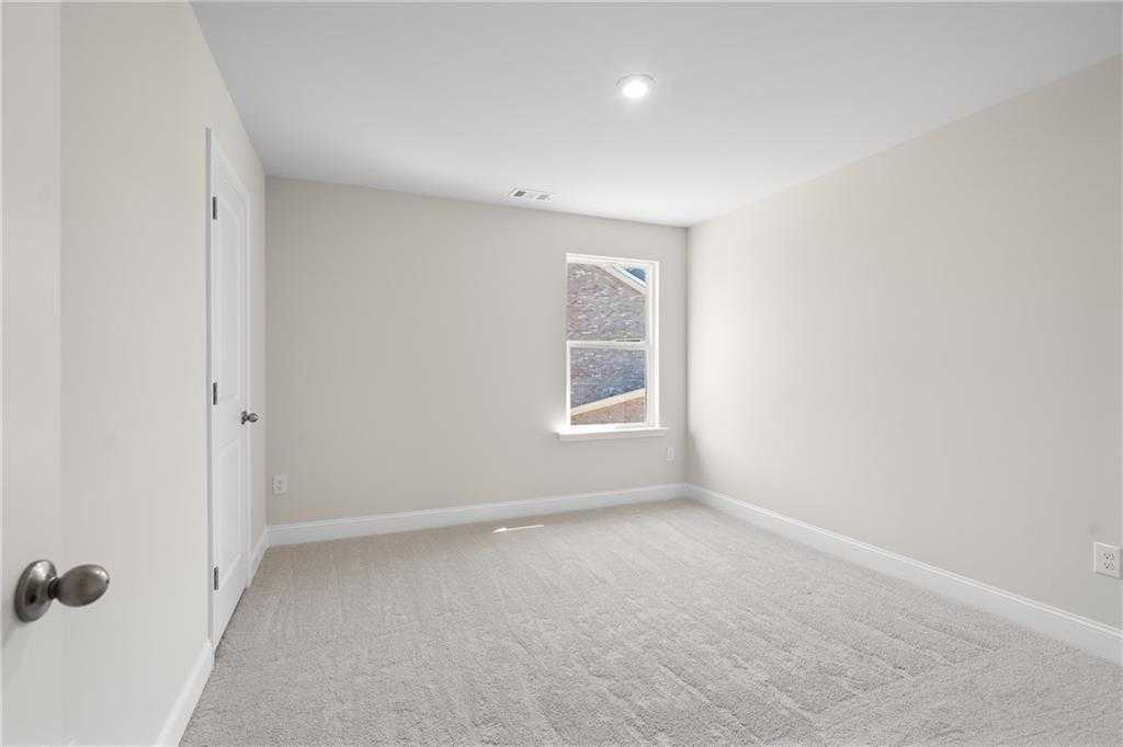Empty secondary bedroom featuring beige walls, plush carpet, and large window in The Hickory B home, Buford, GA