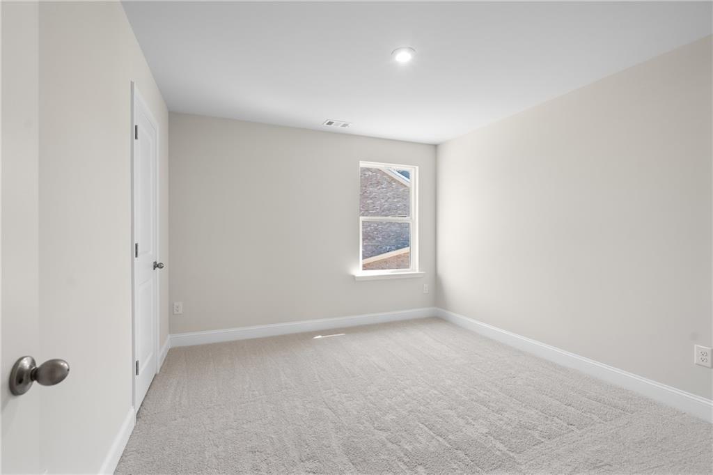 Empty bedroom with beige walls, neutral carpet, double closet doors, and window in Davidson Homes The Hickory E, Buford, GA