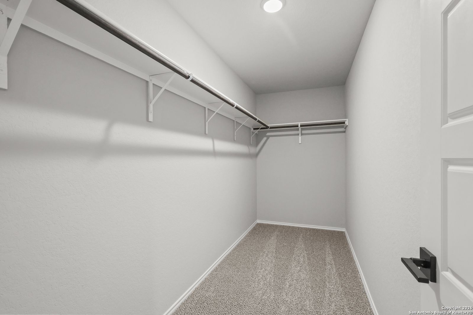 Spacious walk-in closet with gray walls, carpet floor, built-in shelves and rods in Davidson Homes The Murray K, Comanche Ridge, San Antonio