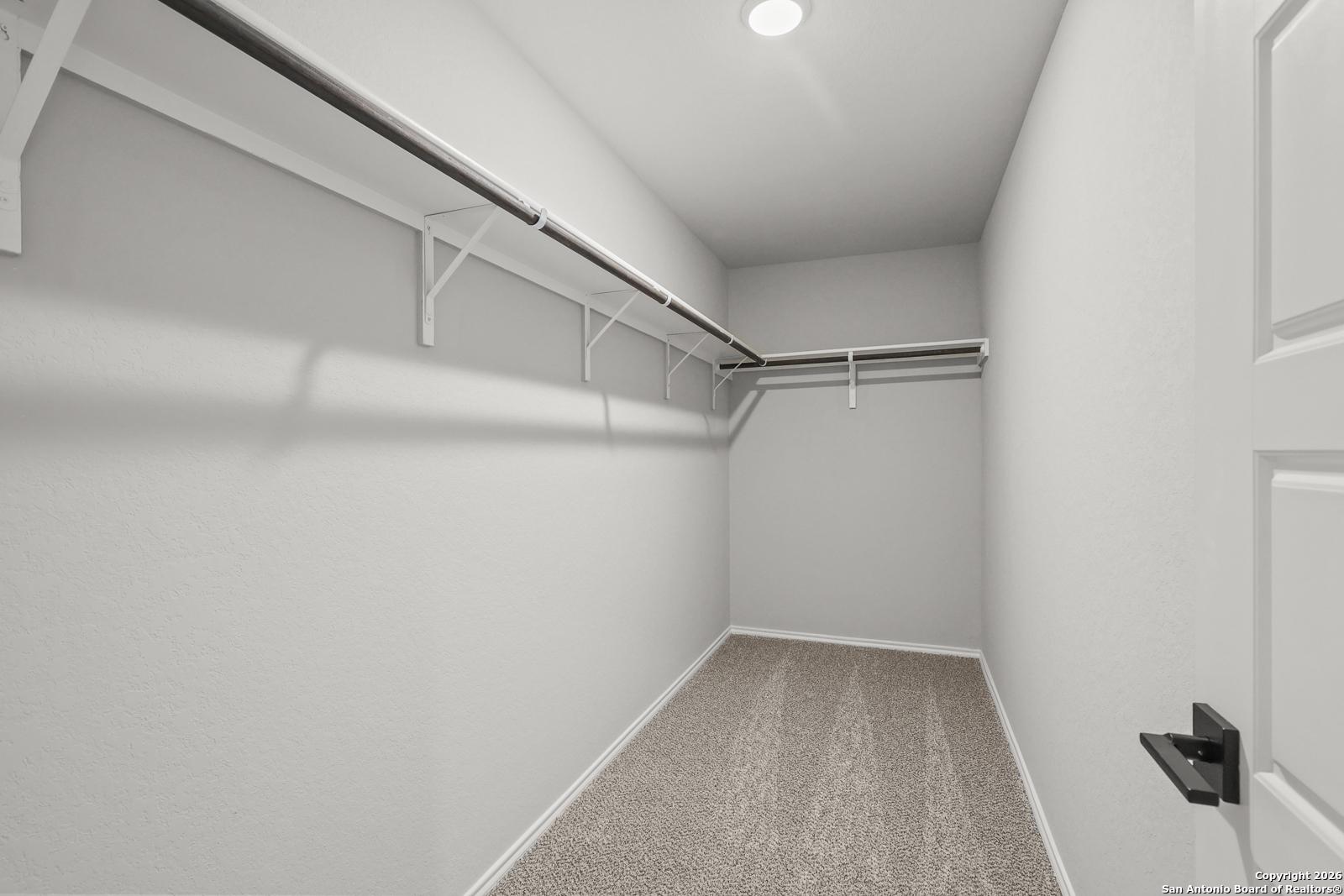 Spacious walk-in closet with gray walls, carpet floor, built-in shelves and rods in Davidson Homes The Murray K, Comanche Ridge, San Antonio