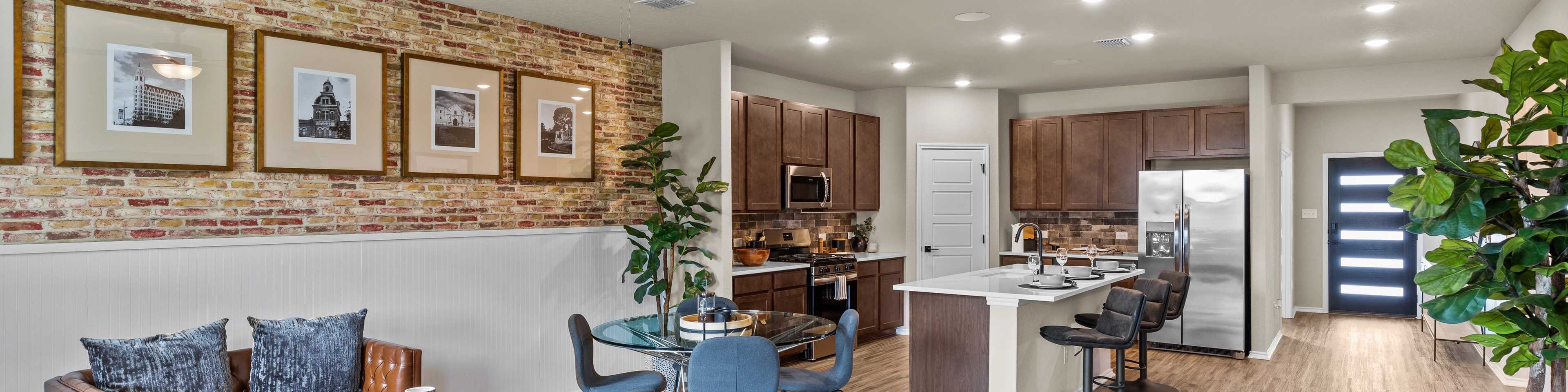 Open-concept kitchen and living room at Morgan Meadows in San Antonio Texas by Davidson Homes with hardwood floors brick accent wall and leather sofa