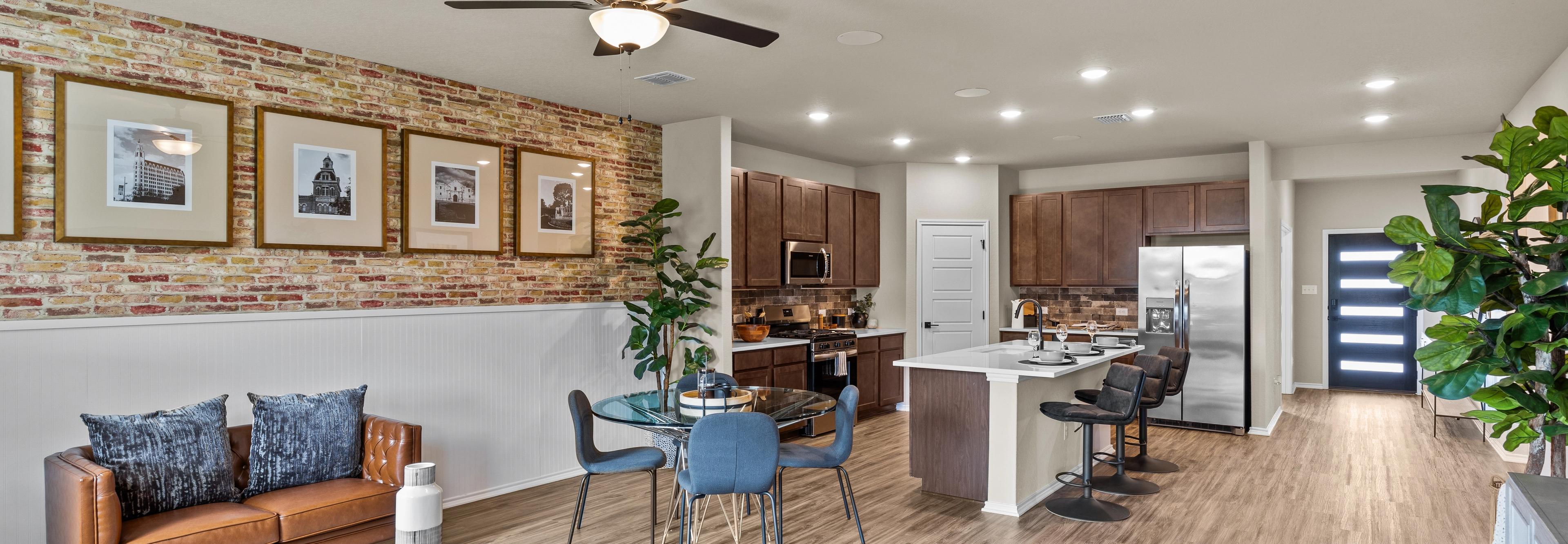 Open-concept kitchen and living room at Morgan Meadows in San Antonio Texas by Davidson Homes with hardwood floors brick accent wall and leather sofa