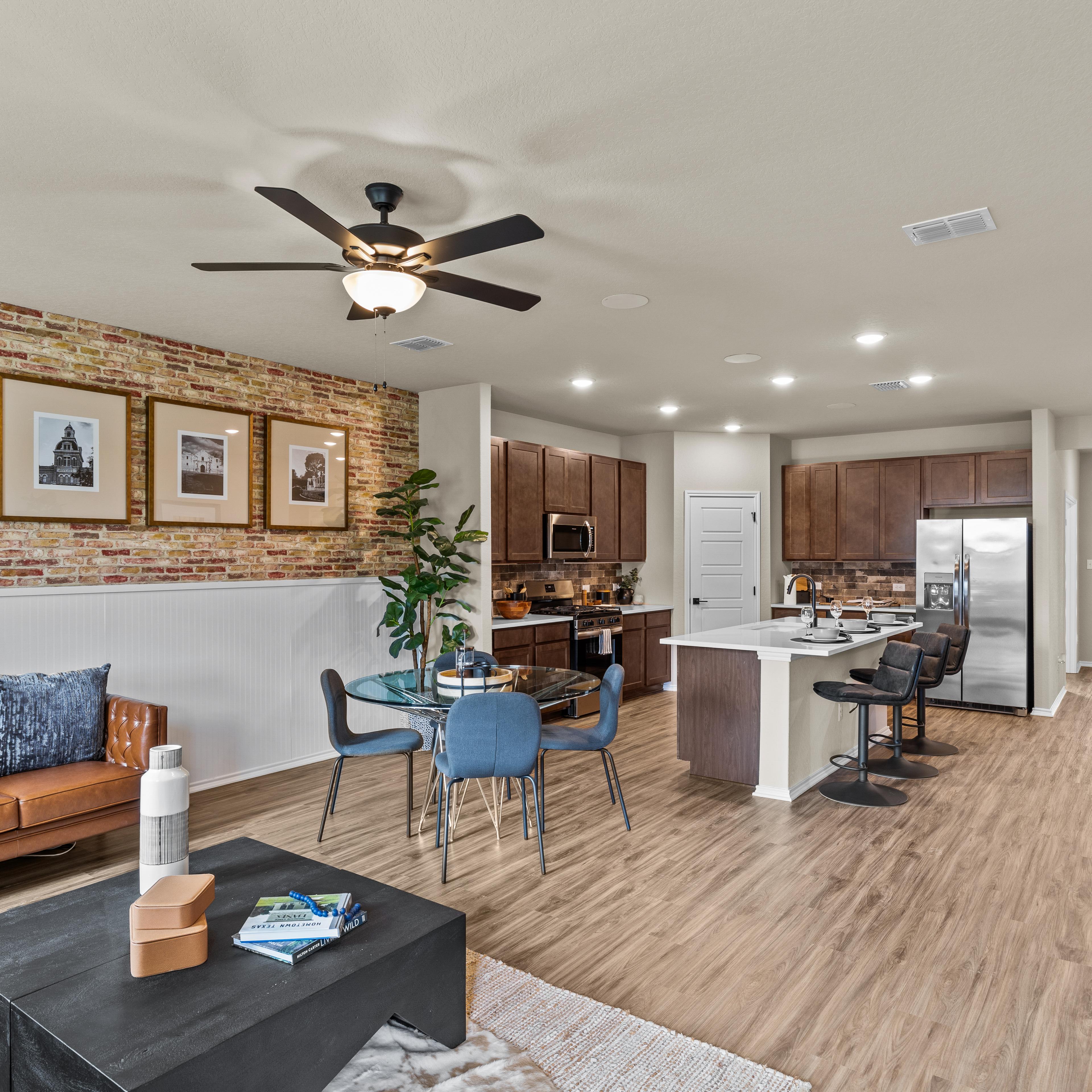 Open-concept kitchen and living room at Morgan Meadows in San Antonio Texas by Davidson Homes with hardwood floors brick accent wall and leather sofa
