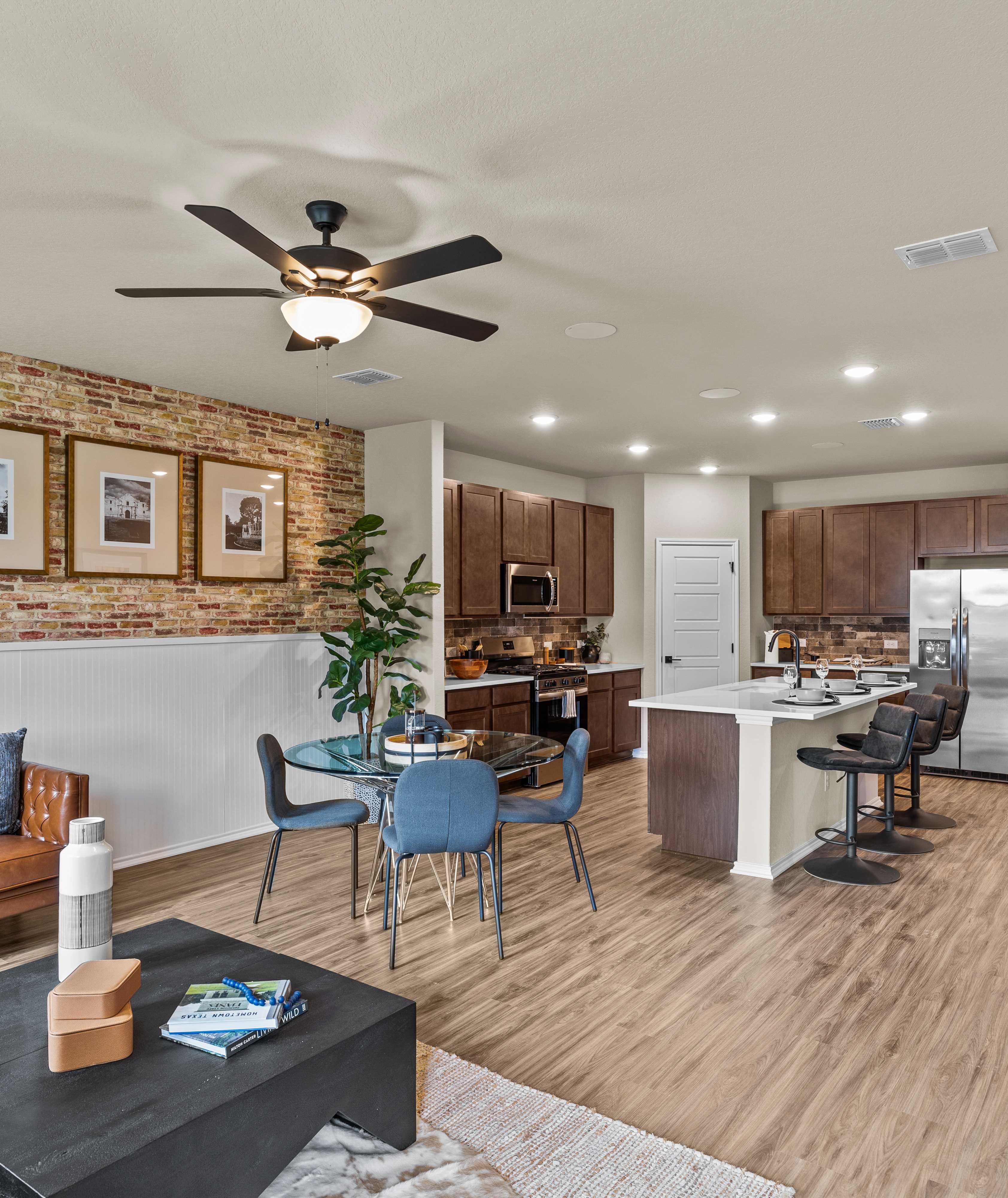 Open-concept kitchen and living room at Morgan Meadows in San Antonio Texas by Davidson Homes with hardwood floors brick accent wall and leather sofa