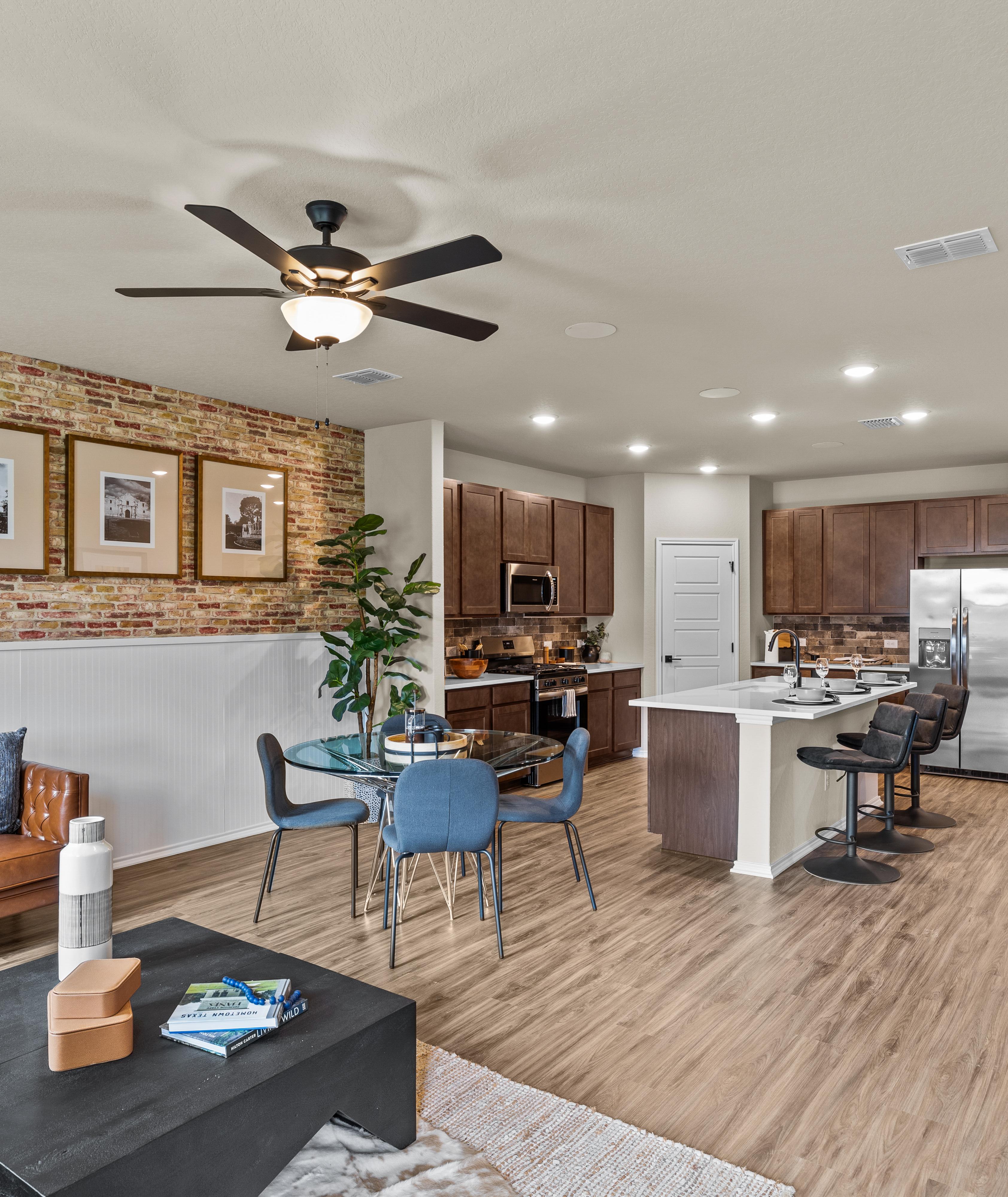 Open-concept kitchen and living room at Morgan Meadows in San Antonio Texas by Davidson Homes with hardwood floors brick accent wall and leather sofa