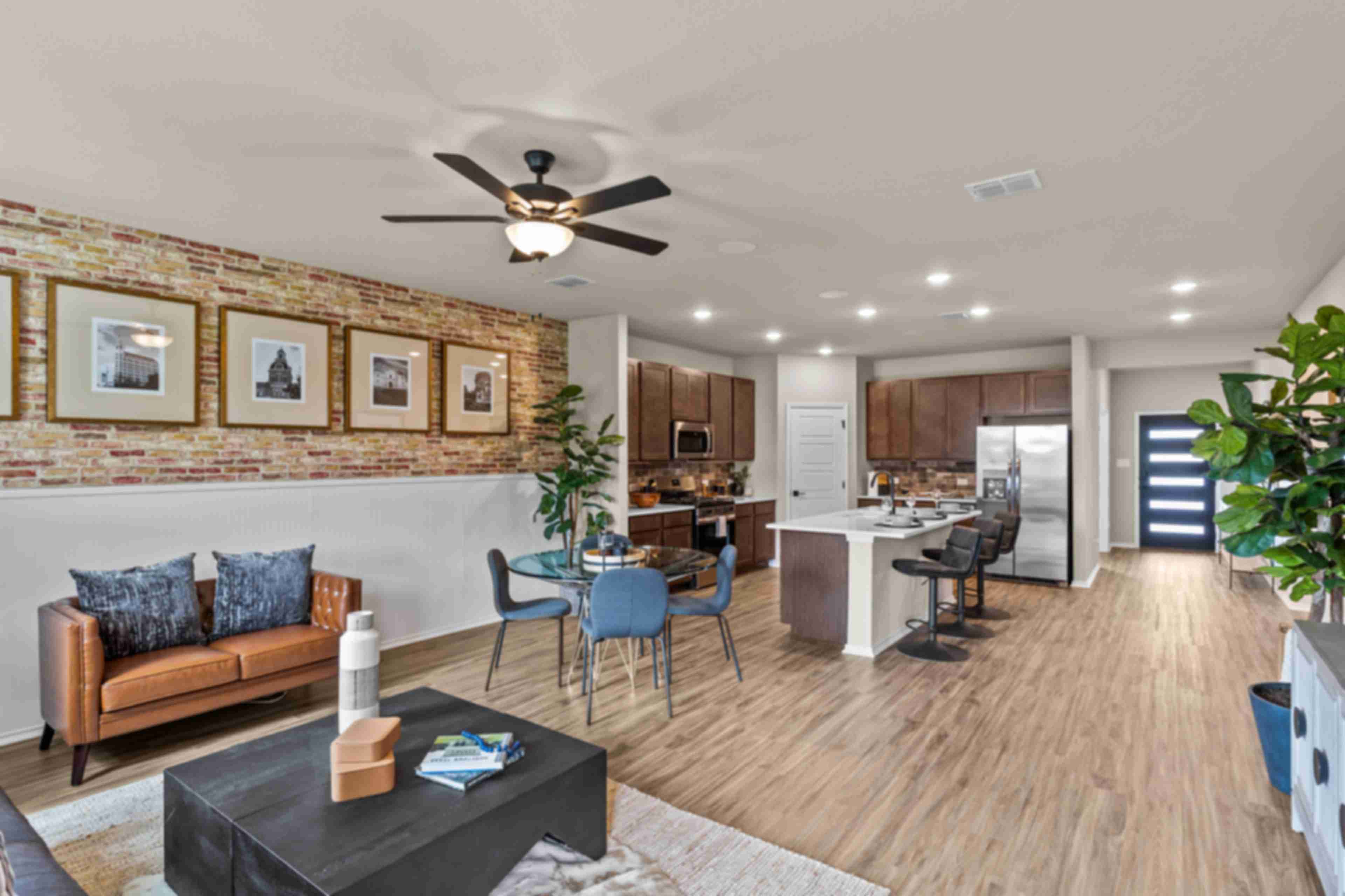 Open-concept kitchen and living room at Morgan Meadows in San Antonio Texas by Davidson Homes with hardwood floors brick accent wall and leather sofa