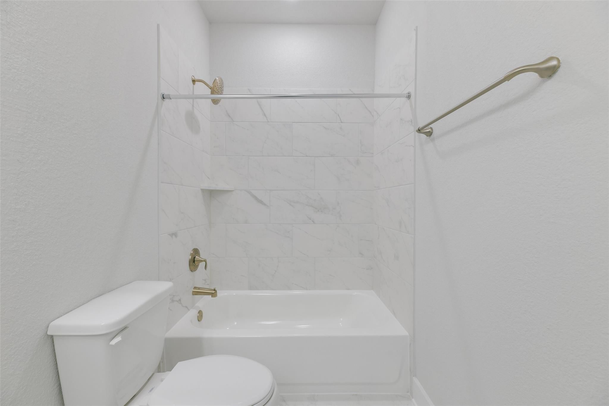 Modern white bathroom featuring subway tile shower enclosure, deep soaking tub, brass fixtures, and grab bars in Davidson Homes The Edward A, Lago Mar