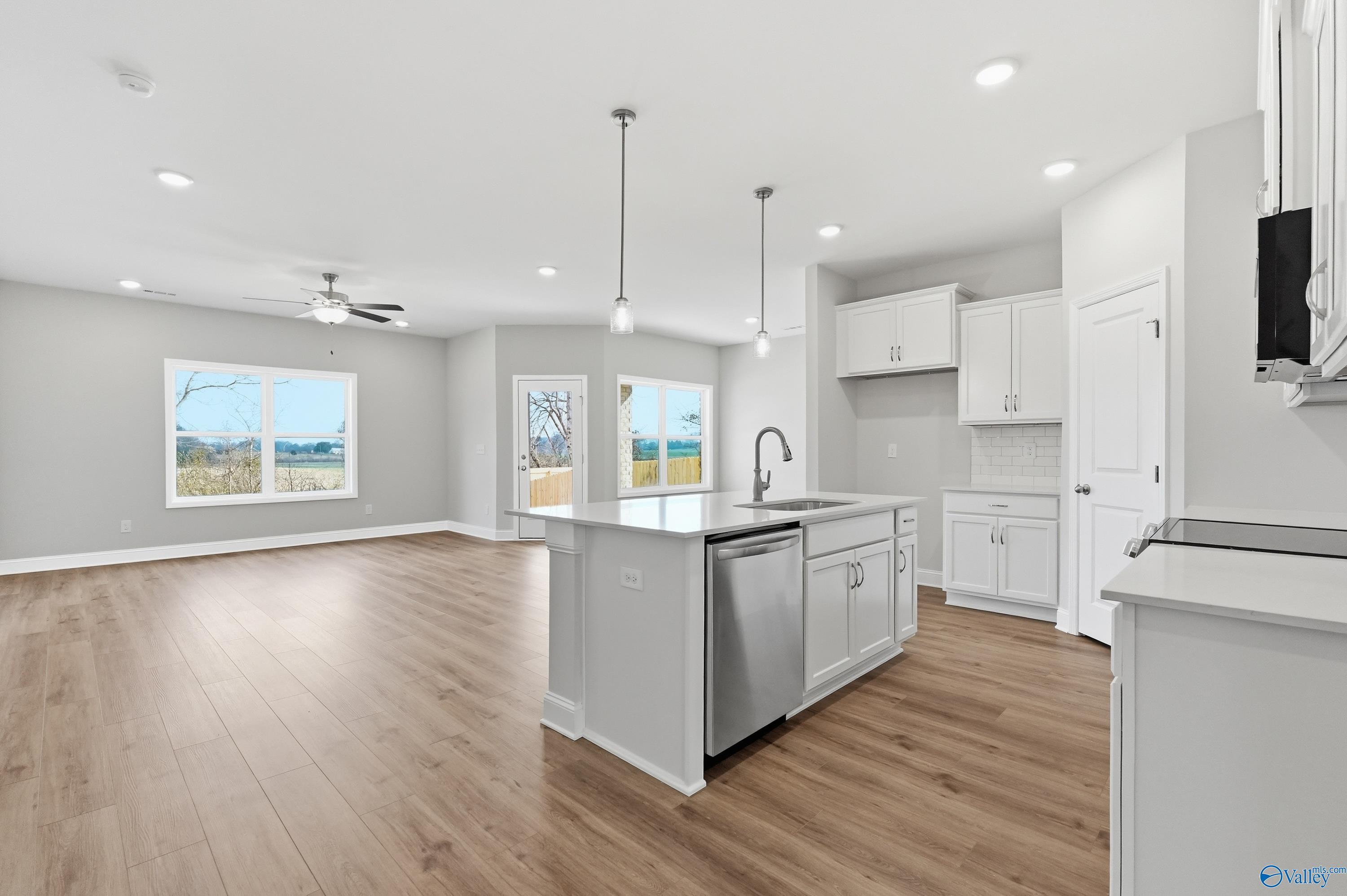 Modern open-concept kitchen with white island, stainless appliances, hardwood floors, and backyard views in Davidson Homes The Daphne C, Toney, Alabama