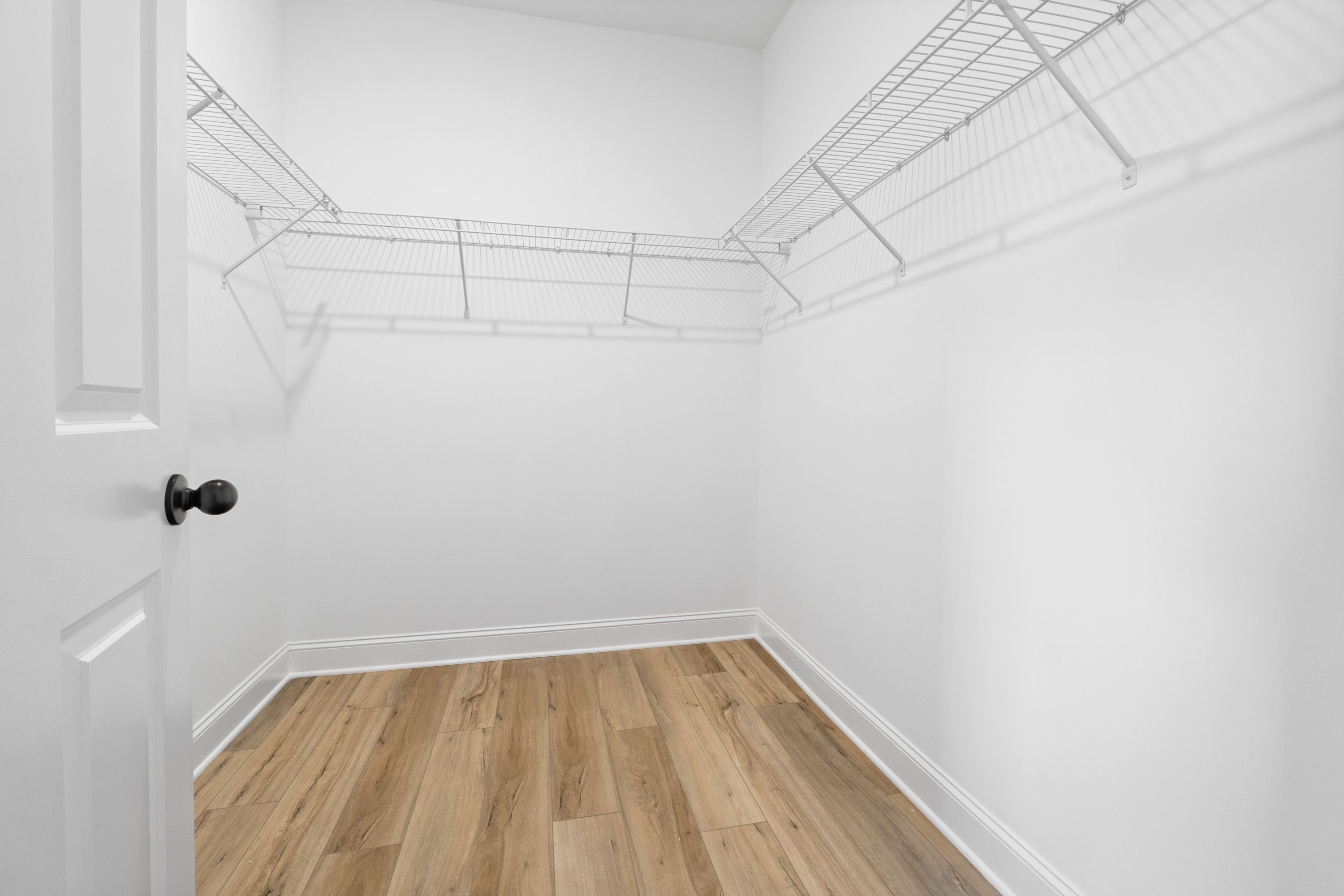 Spacious walk-in closet in The Valencia master suite with wire shelving, white walls, and hardwood floors