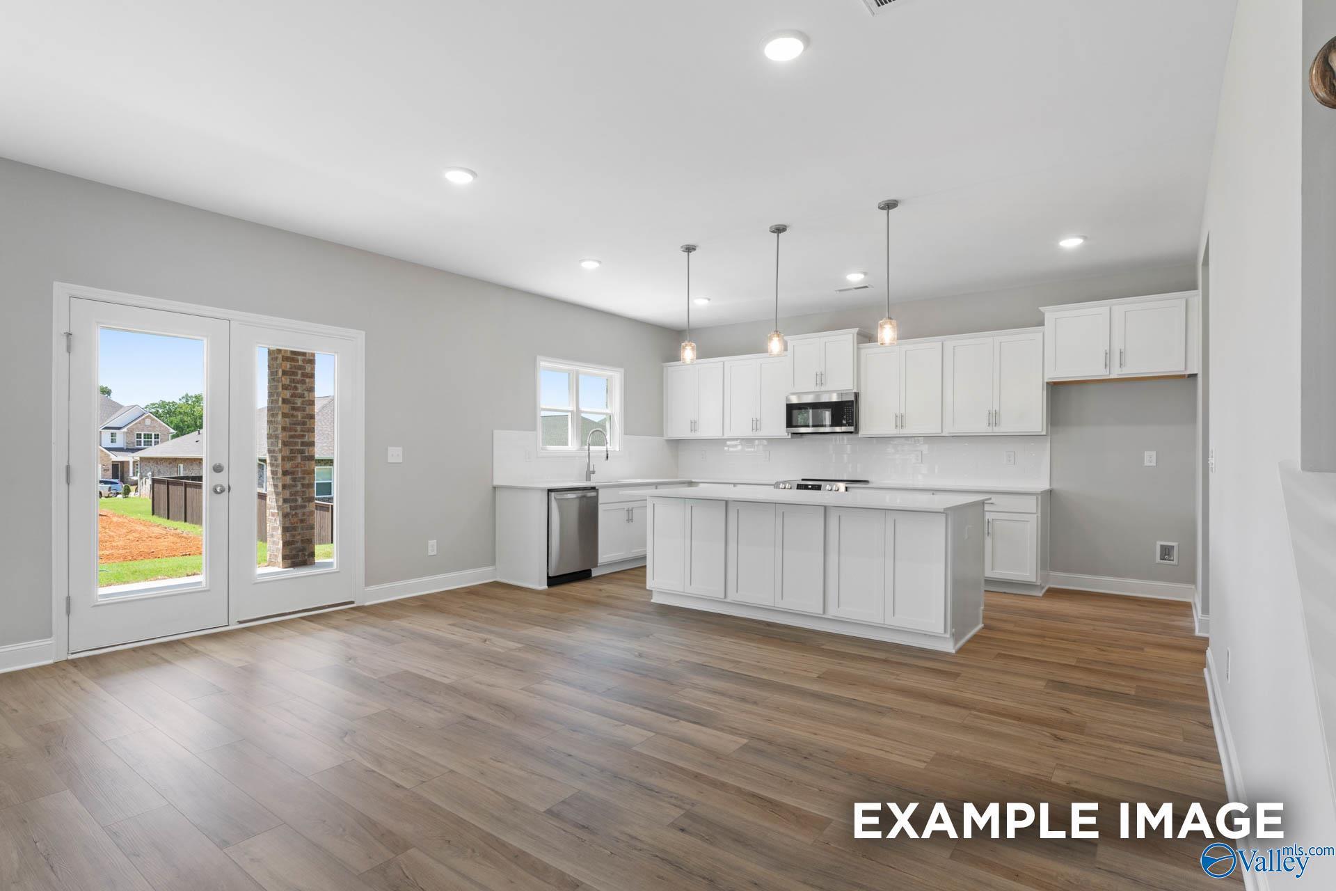 Modern white kitchen with island, stainless appliances, pendant lights, hardwood floors, and French doors to backyard in The Chelsea B home, New Market, AL