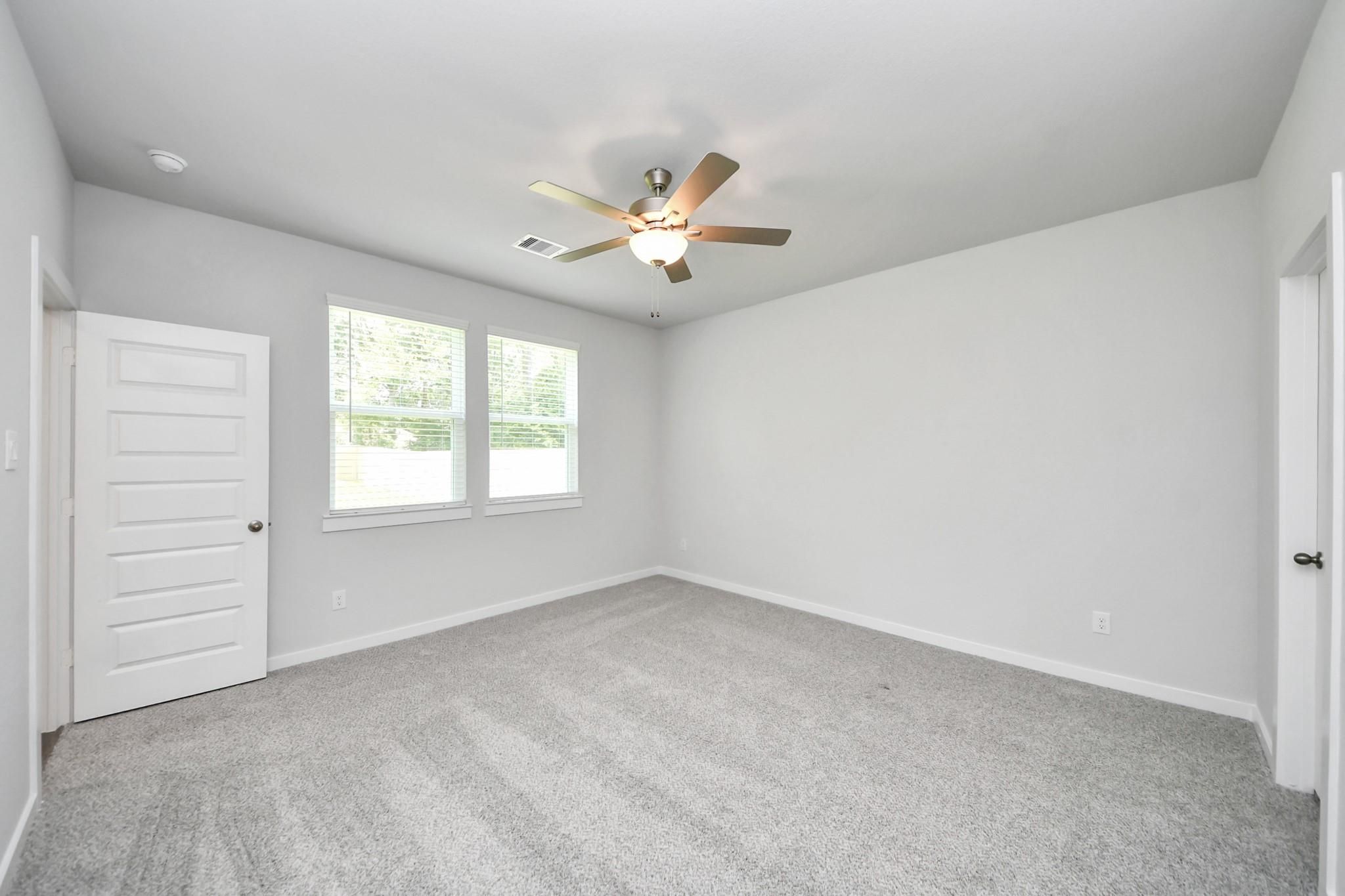 Spacious bedroom with grey carpet and ceiling fan in The Sabine E floor plan at Liberty Estates, Cleveland, Texas.