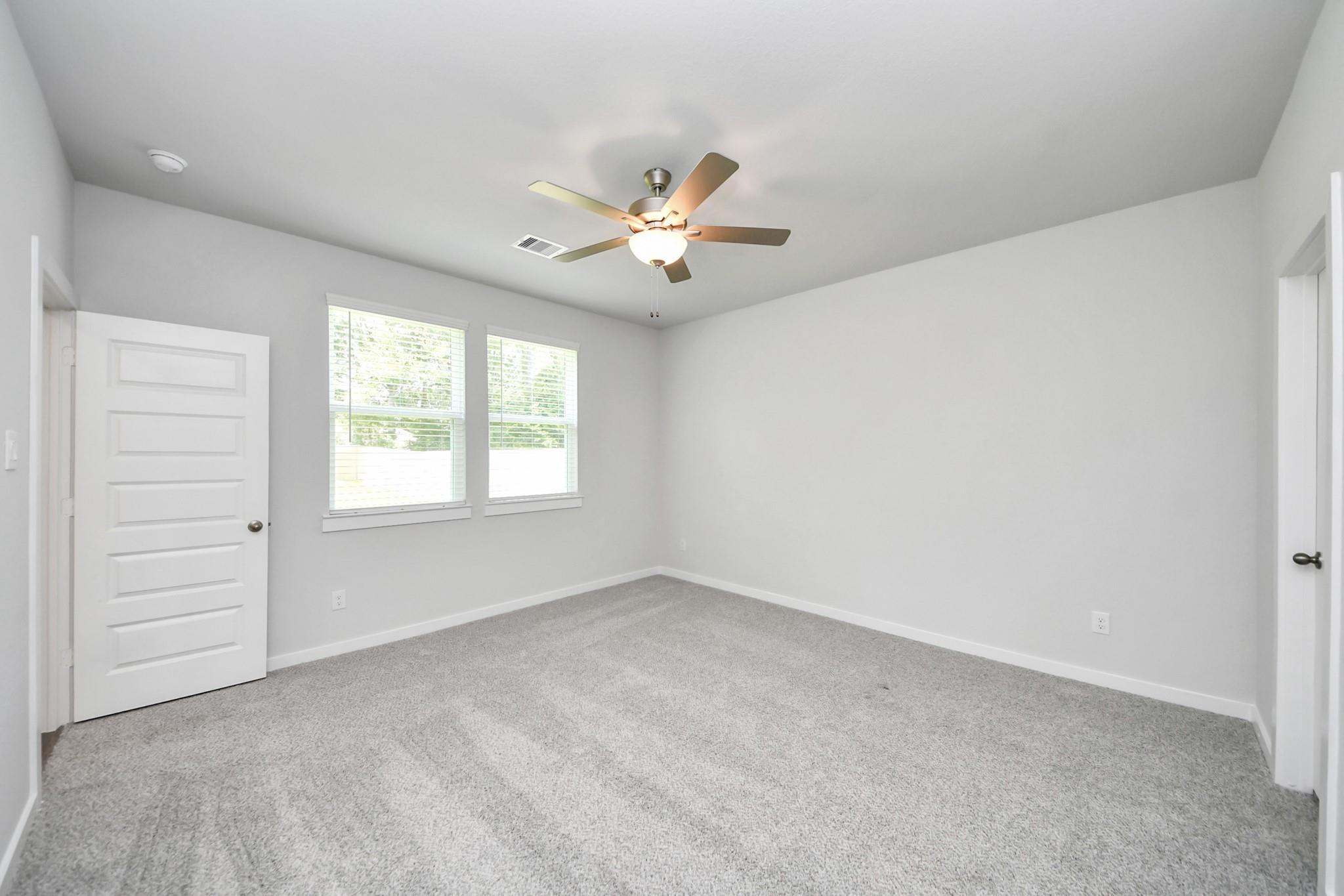 Spacious bedroom with grey carpet and ceiling fan in The Sabine E floor plan at Liberty Estates, Cleveland, Texas.