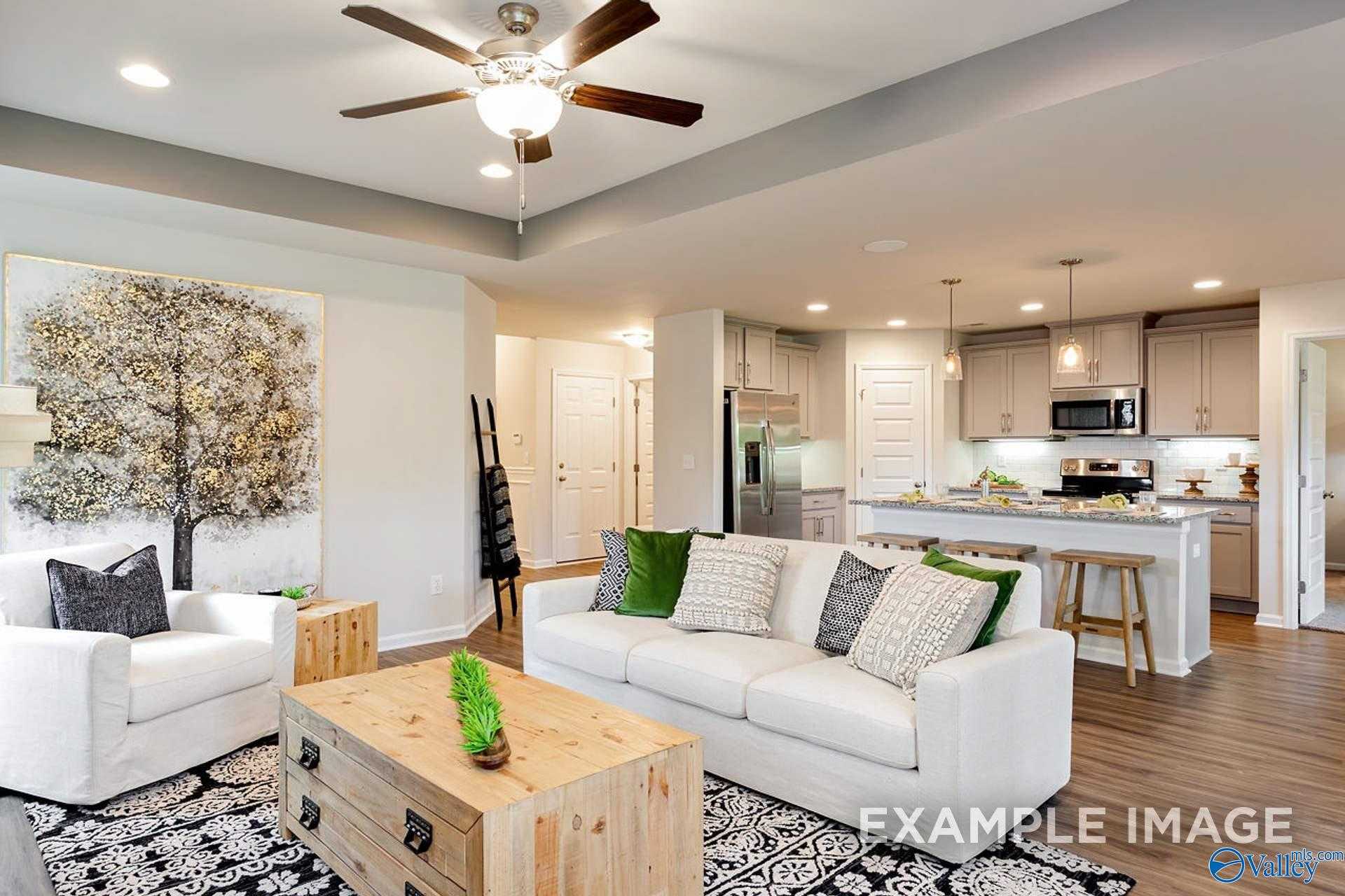 Open-concept living room with white sectional sofa, abstract tree artwork, and adjacent modern kitchen in Davidson Homes The Franklin B, Hazel Green, Alabama
