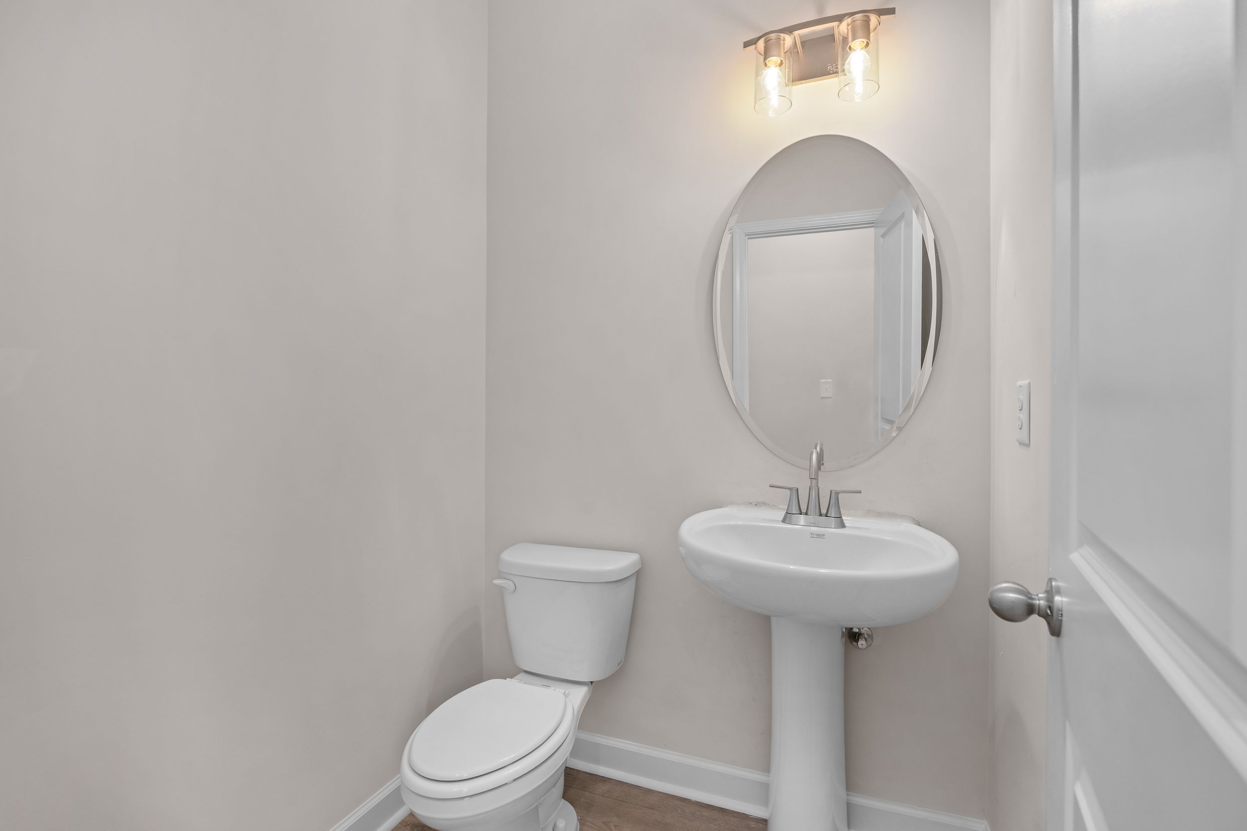 Elegant powder room at Forestville Yard Townhomes in Knightdale NC with pedestal sink, round mirror and sconce lighting