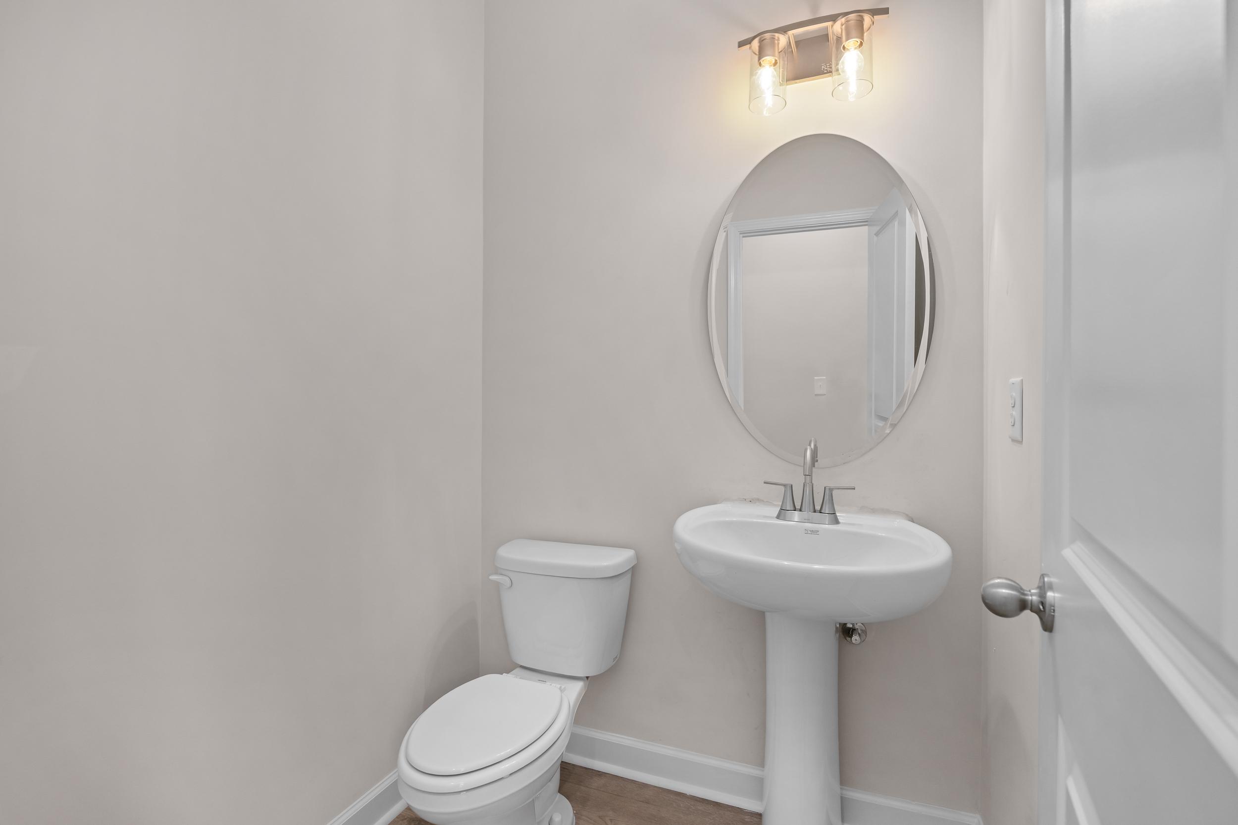 Elegant powder room at Forestville Yard Townhomes in Knightdale NC with pedestal sink, round mirror and sconce lighting