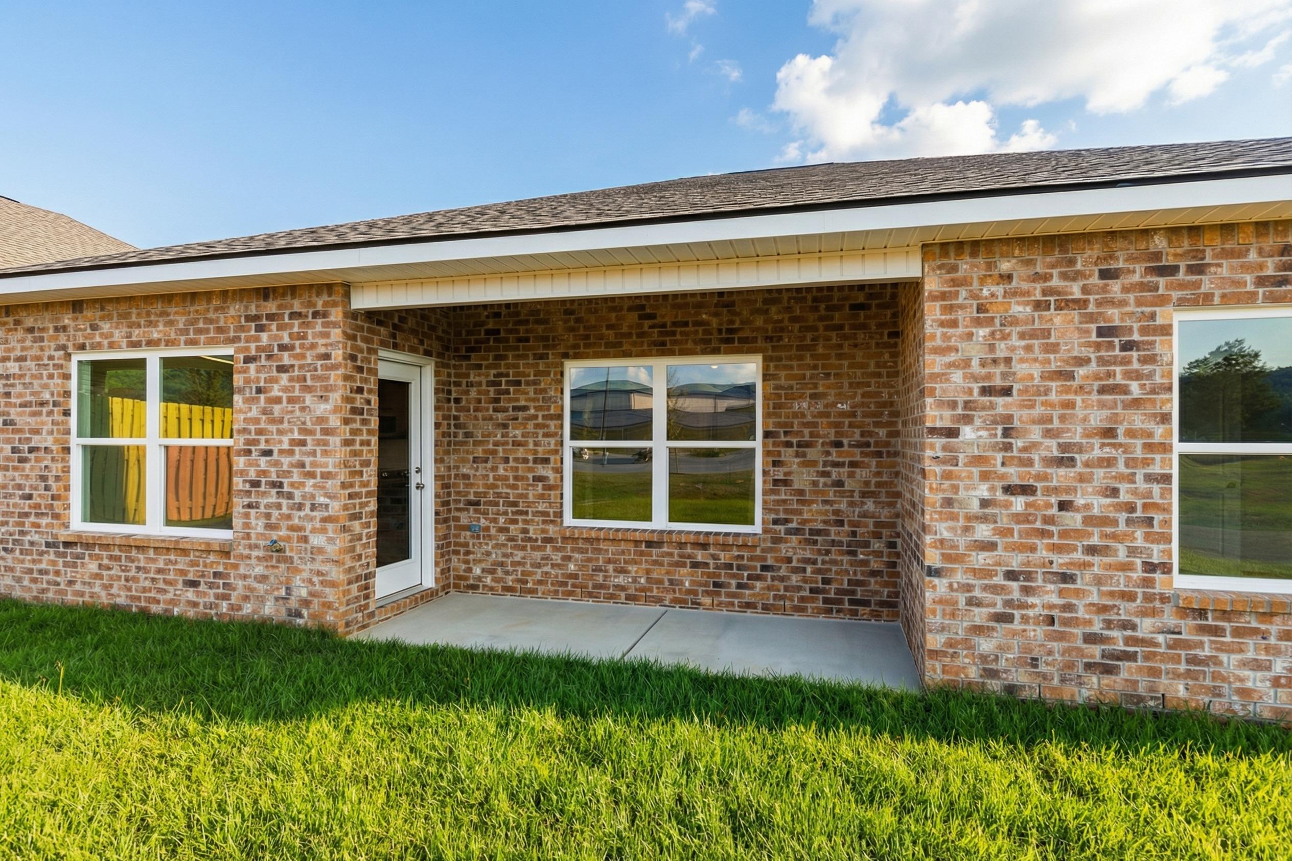 Brick home side exterior at Mooresville Station in Tanner Alabama with covered porch, large windows, and lush green lawn