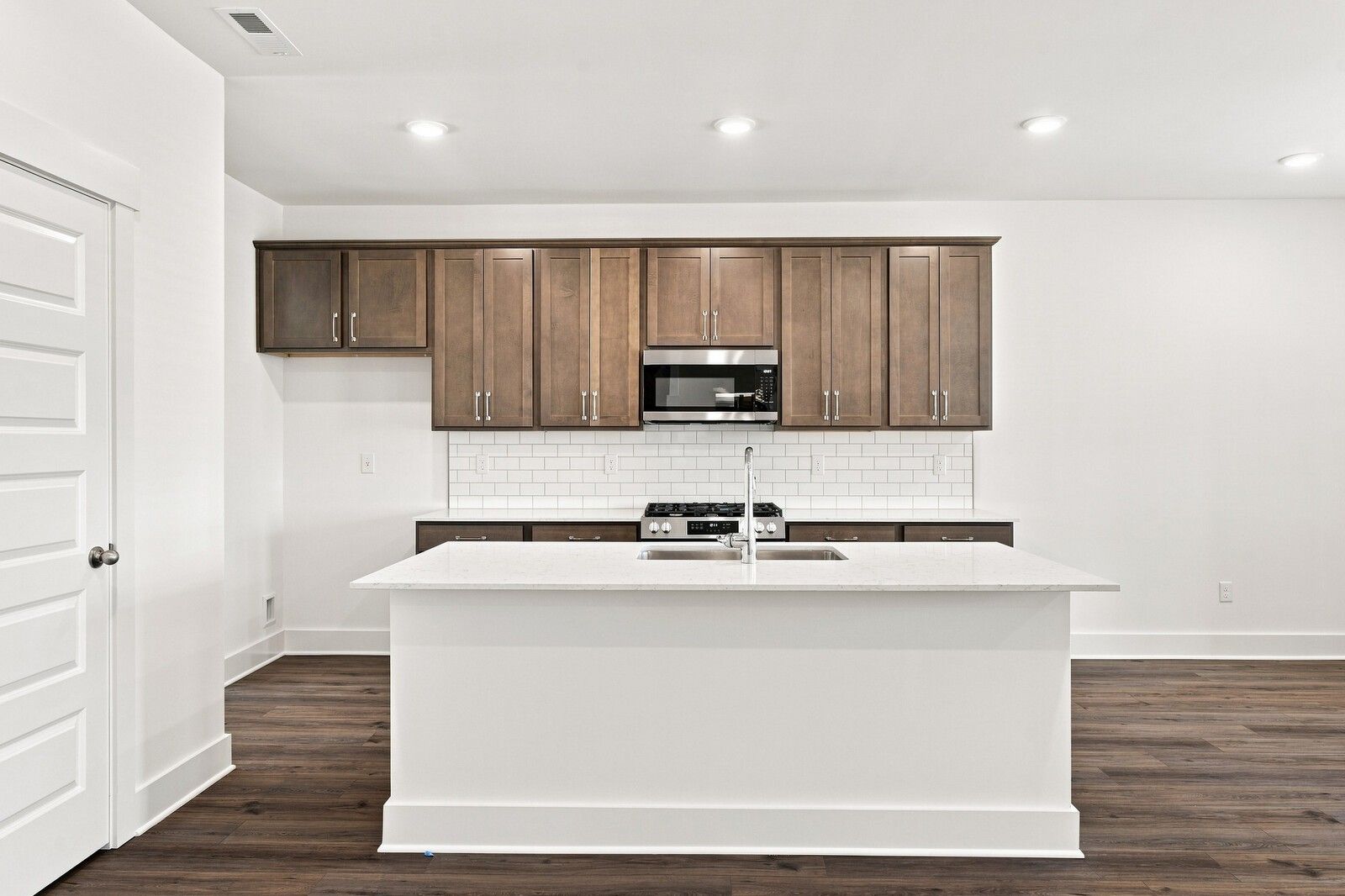 White kitchen island with sink, dark wood cabinets, subway tile backsplash, and stainless appliances in Davidson Homes Gallatin home