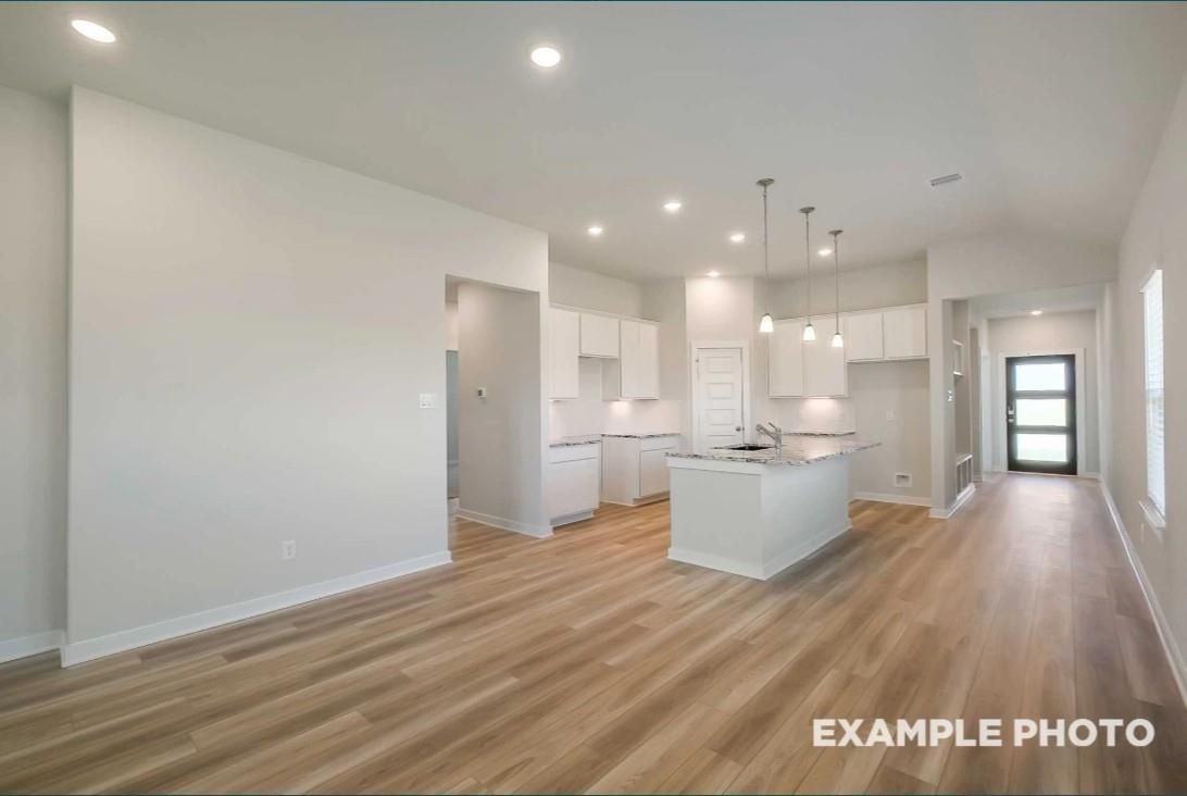 Open-concept kitchen with white cabinets, large center island, and luxury vinyl plank floors in Davidson Homes Riviera C, Dayton TX