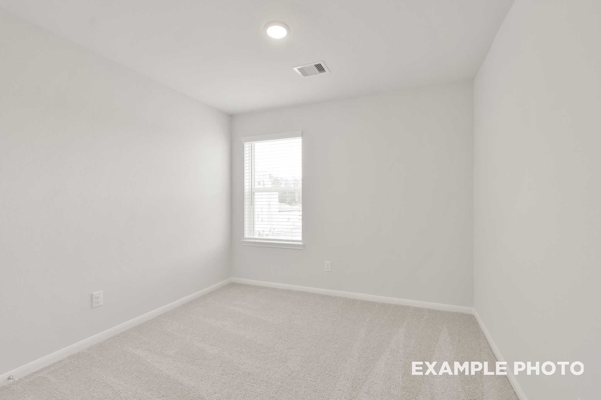 Bright empty bedroom with white walls, carpet flooring, and window with blinds in The Brazos by Davidson Homes, Beasley TX
