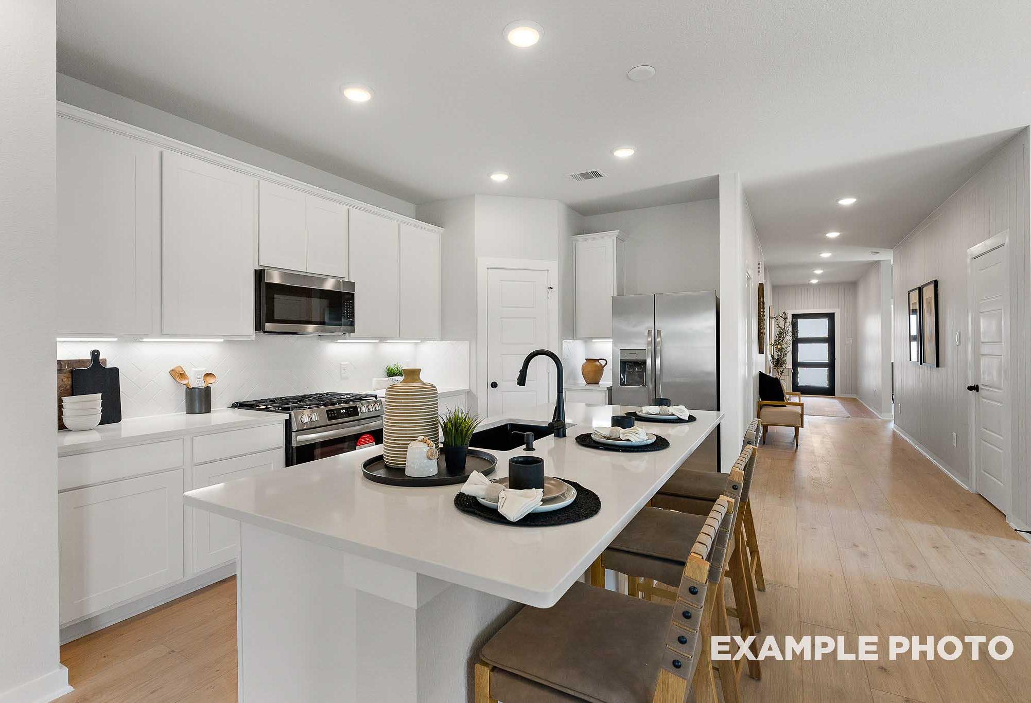 Spacious modern kitchen in The Everett C with white shaker cabinets, large quartz island, stainless steel appliances, and open hallway