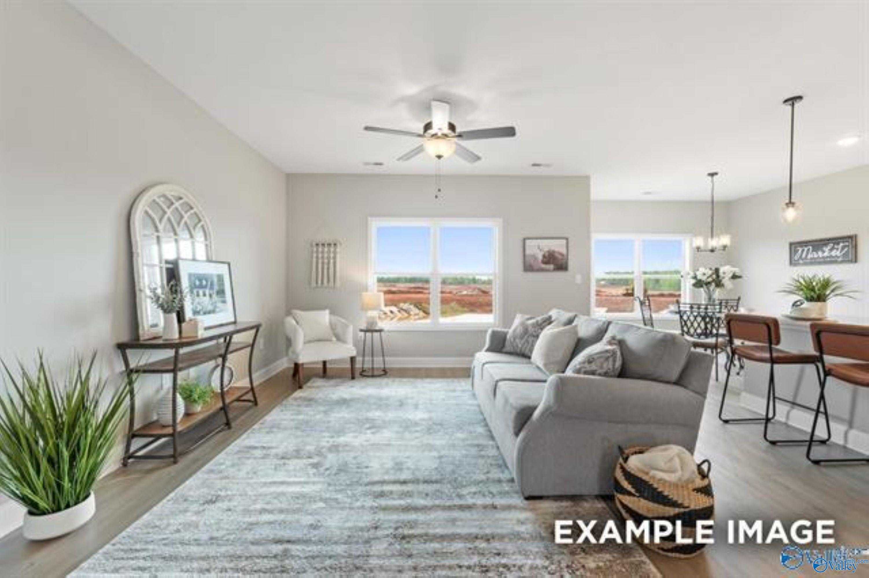 Open living room with gray sectional sofa, arched mirror, plants, and large windows in The Asheville 3-bedroom home, Owens Cross Roads, Alabama