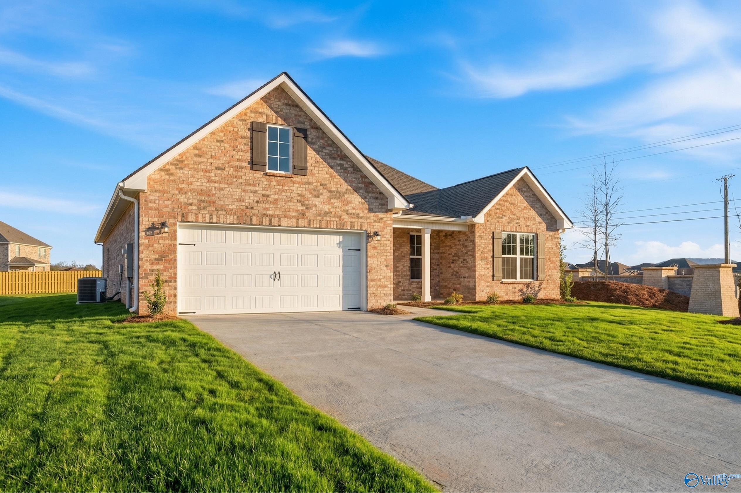 Single-story brick ranch home with 2-car garage, covered porch, lush green lawn, and driveway in Davidson Homes Creekside, Harvest, Alabama