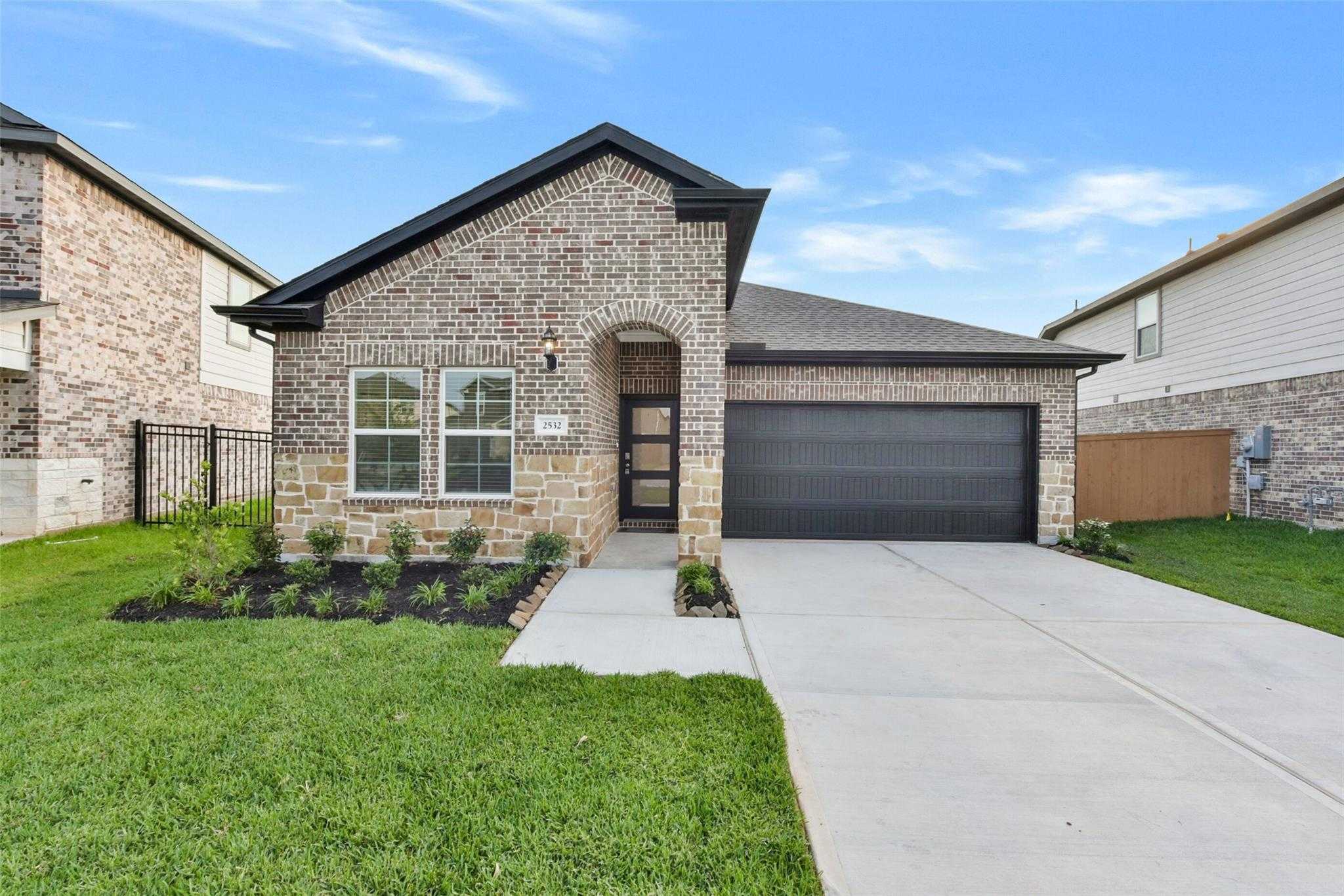 Modern brick 1-story home with stone accents, 2-car garage, driveway, and lush landscaping in Sunterra, Katy, Texas - Davidson Homes Laguna B