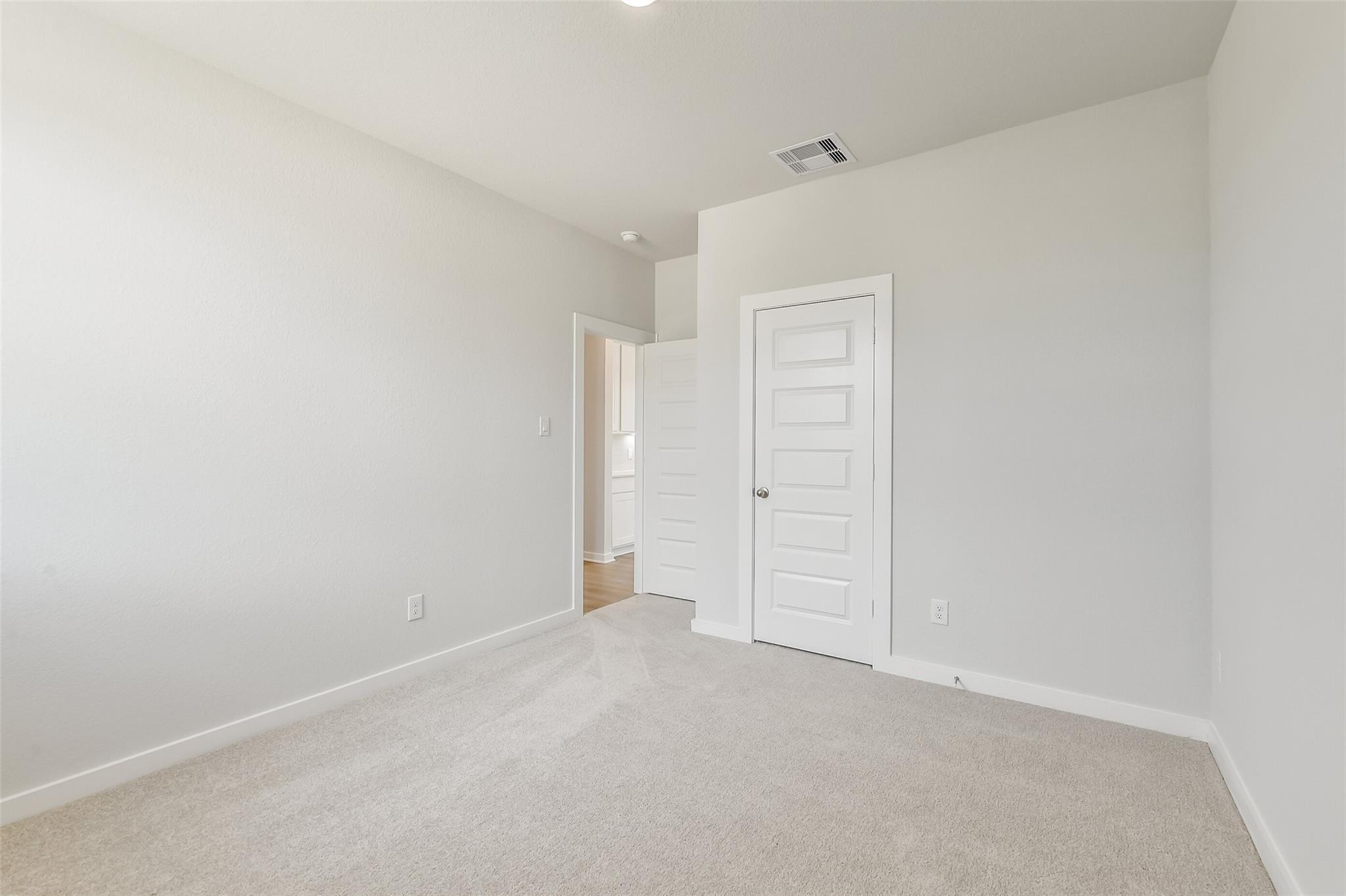 Empty bedroom featuring light gray walls, beige carpet, white doors, and adjacent bathroom in Davidson Homes The Frio G, Conroe, Texas