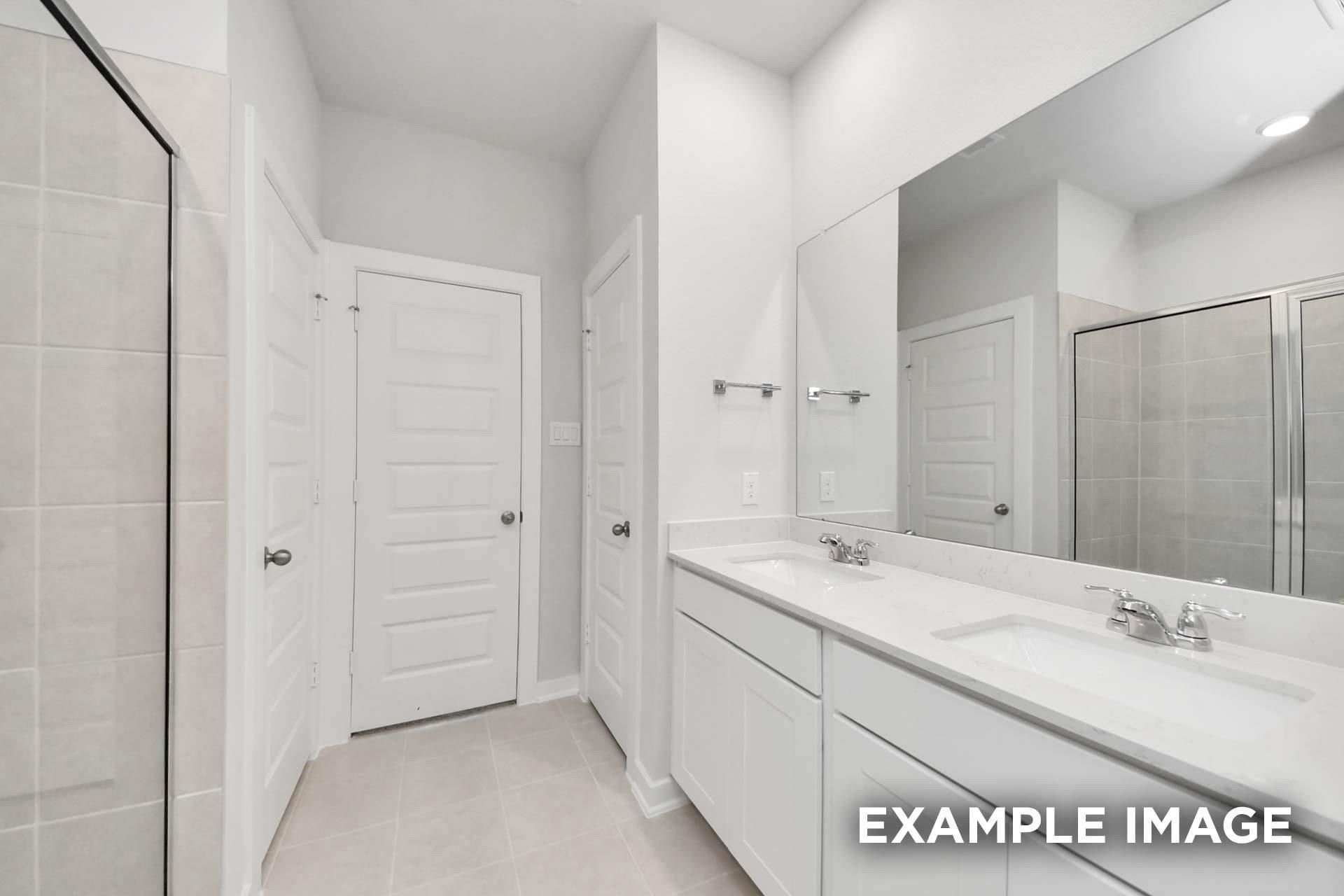 Bright dual-sink bathroom with white vanity, large mirror, and tiled shower in Davidson Homes The Blanco E, Magnolia, Texas