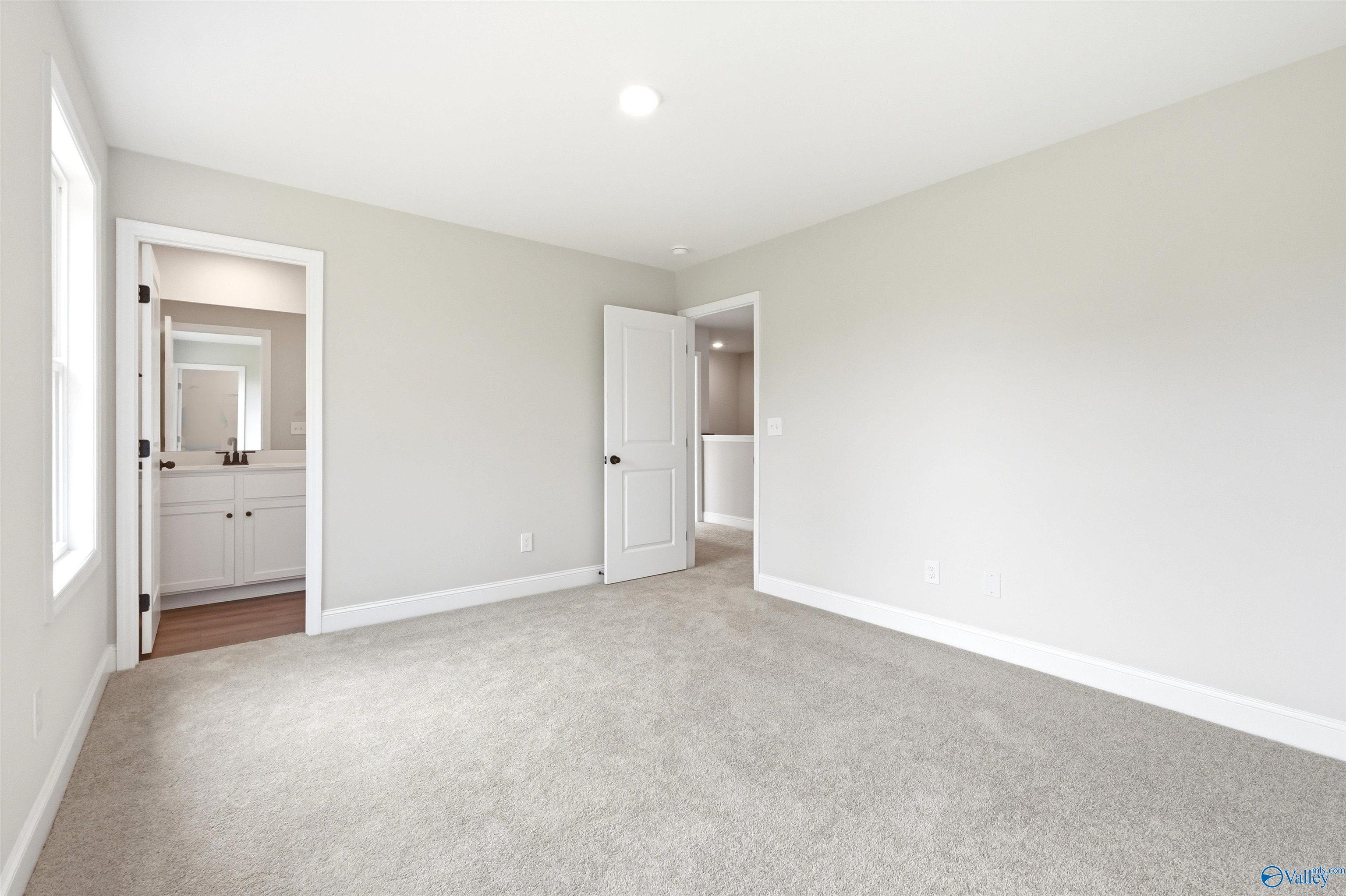 Bright bedroom with neutral carpet and an ensuite bathroom in The Chelsea D floor plan at Berry Cove, New Market, Alabama.