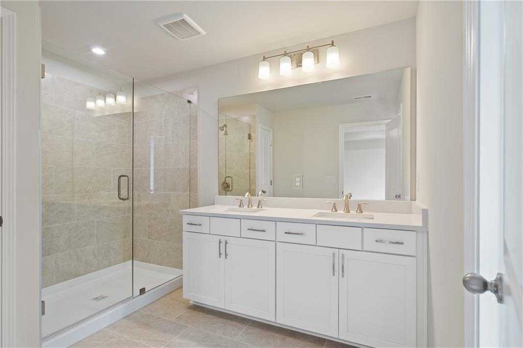 Modern master bathroom featuring double vanity, frameless glass shower, and white cabinets in Davidson Homes The Cary B, Kennesaw, GA