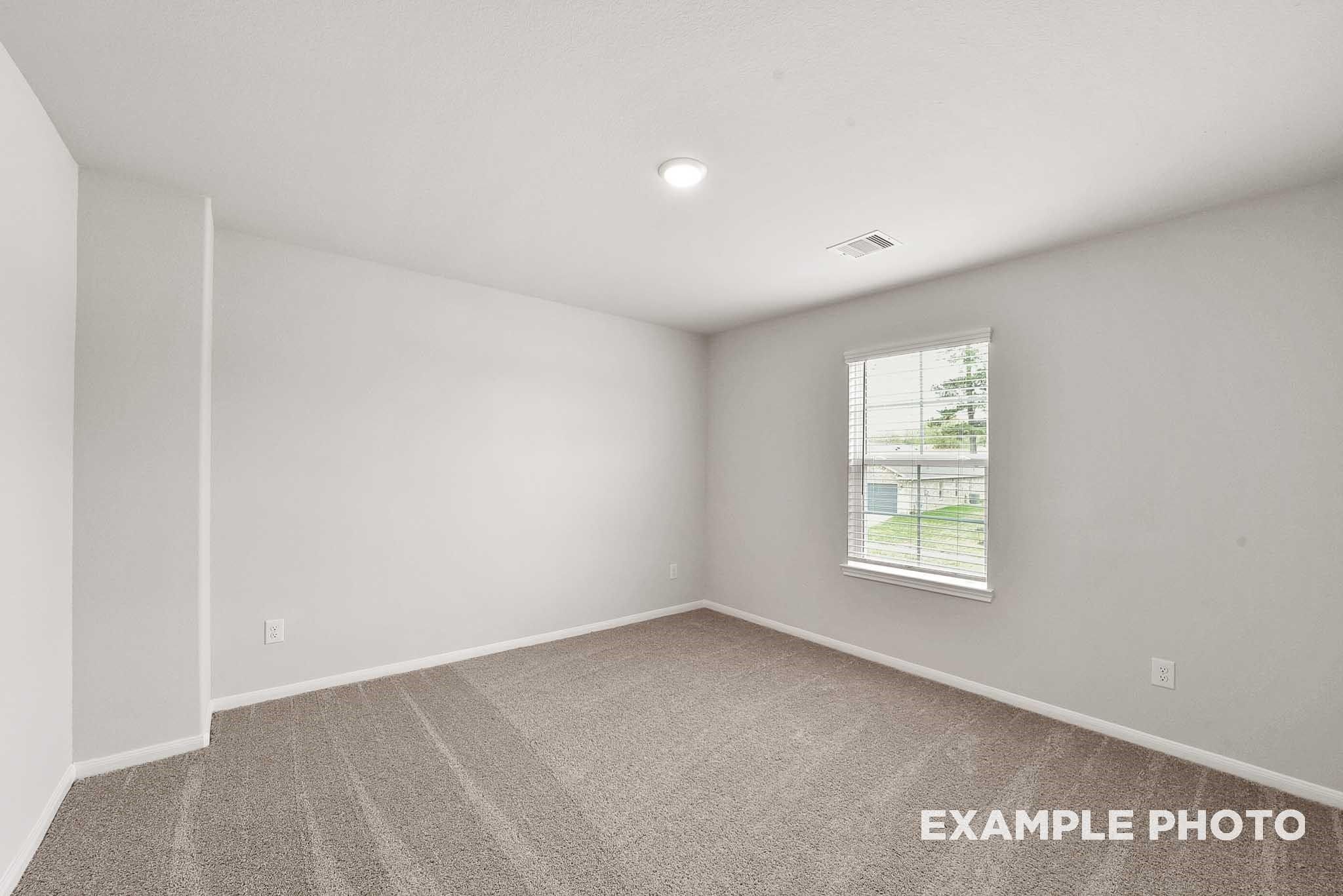 Bright secondary bedroom with neutral walls, carpet floor, and window overlooking yard in Davidson Homes Tierra B, Beasley, Texas