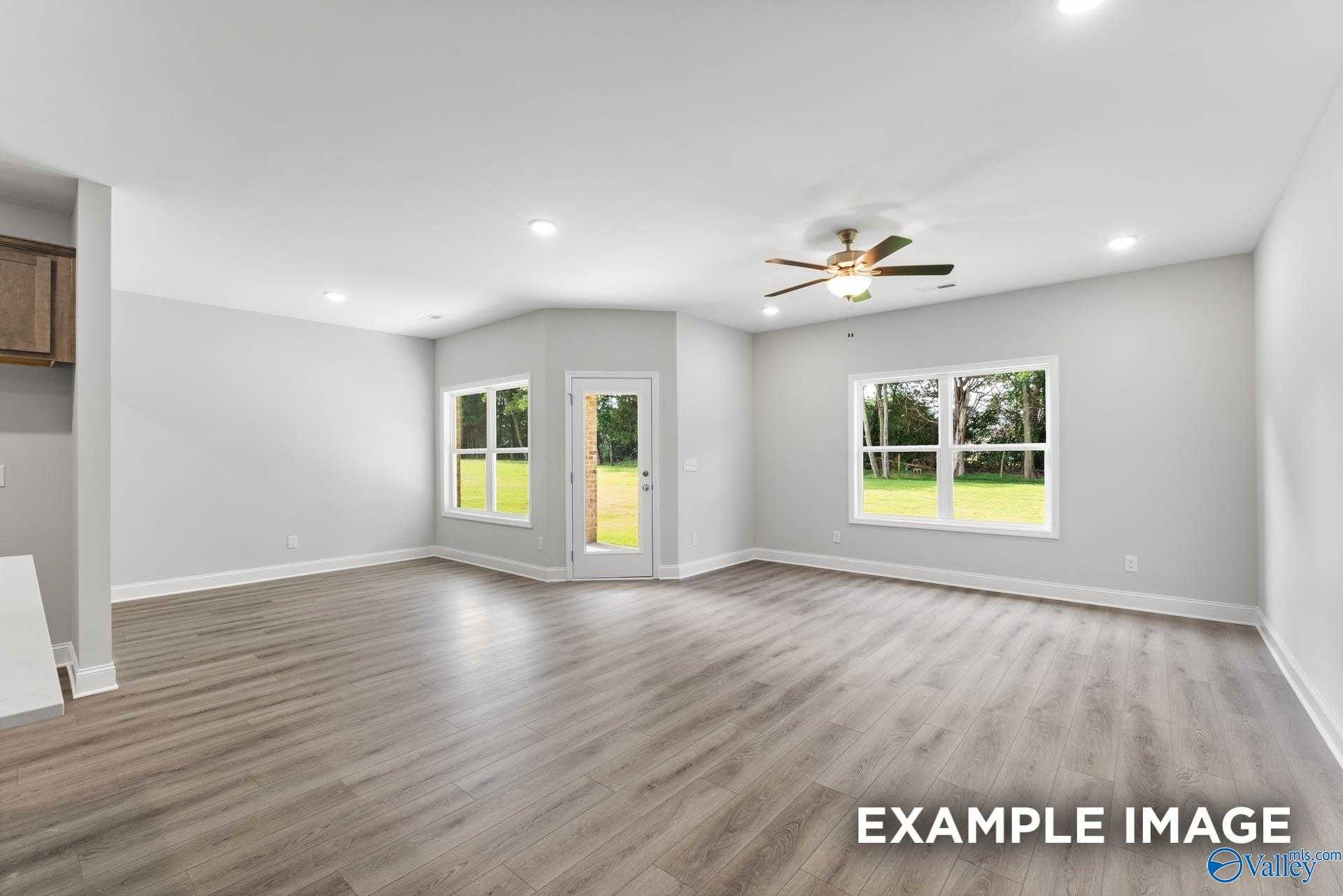 Bright open living room with ceiling fan, large windows, French door to lush backyard in 4-bedroom Davidson Homes The Daphne C, Arab, Alabama