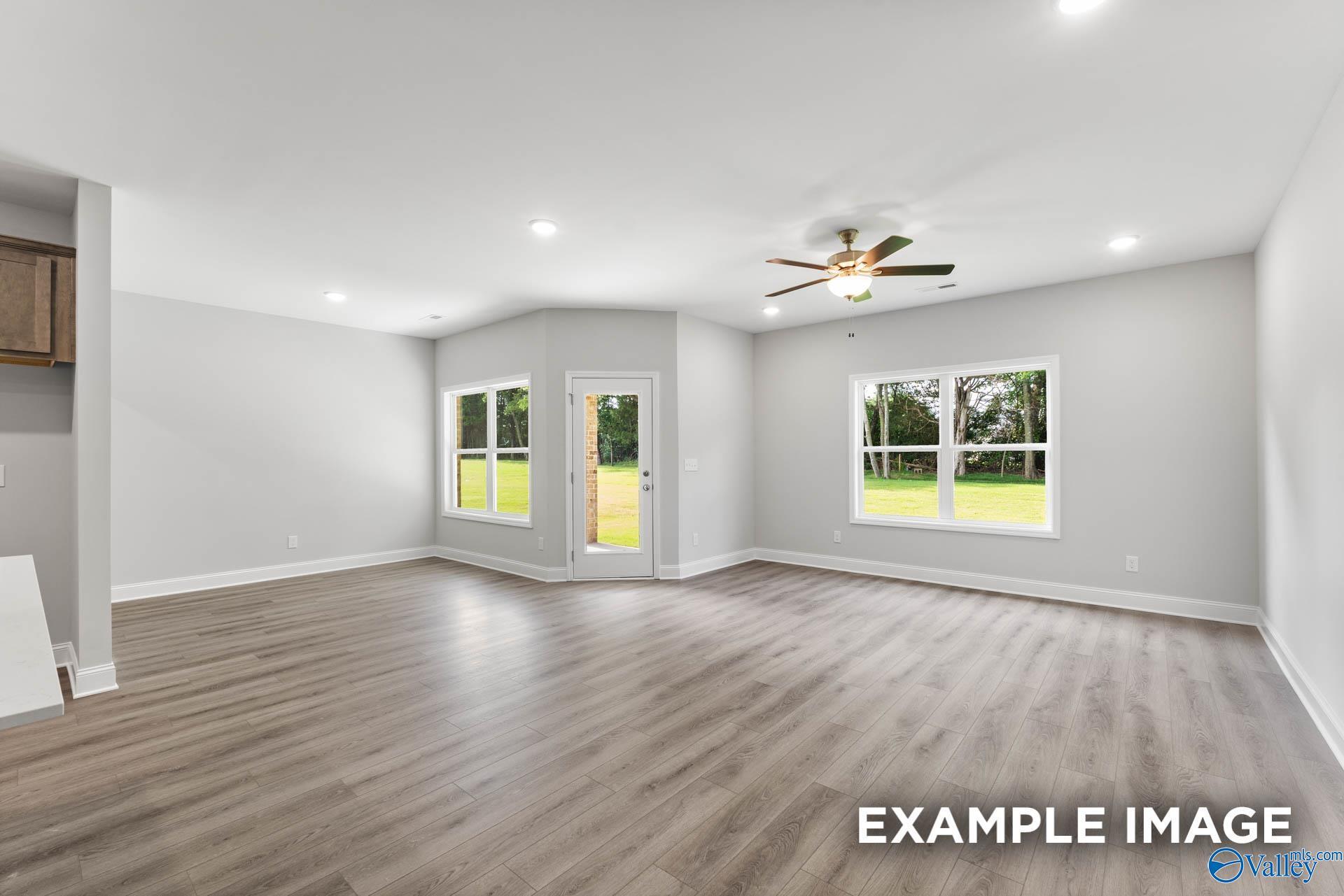 Bright open-concept living room with luxury vinyl plank flooring, ceiling fan, and backyard views in The Daphne, Meridianville, AL