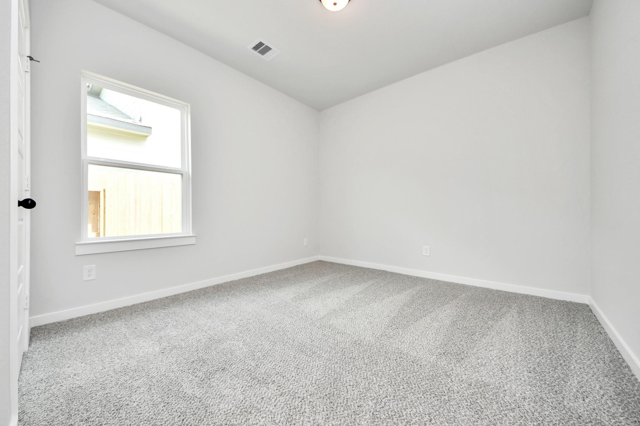 Bright, carpeted bedroom with neutral walls in The Sorrento E floor plan by Davidson Homes in Sundance Cove, Crosby, Texas.