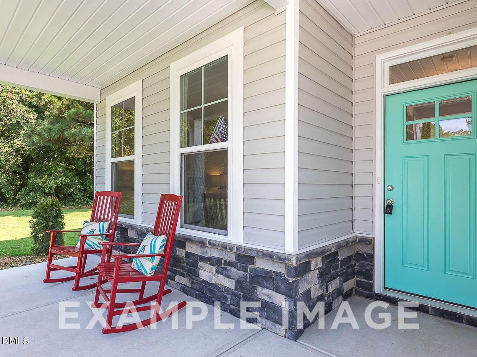 Charming front porch with red rocking chairs and teal door on beige-sided Chestnut B home by Davidson Homes in Lillington, North Carolina
