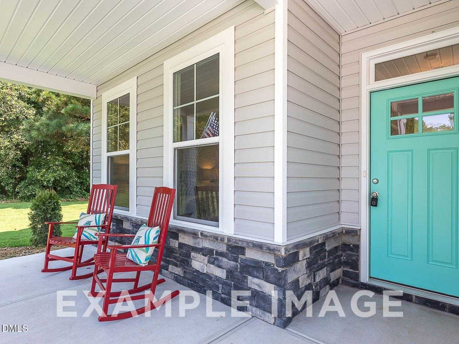 Charming front porch with red rocking chairs and teal door on beige-sided Chestnut B home by Davidson Homes in Lillington, North Carolina