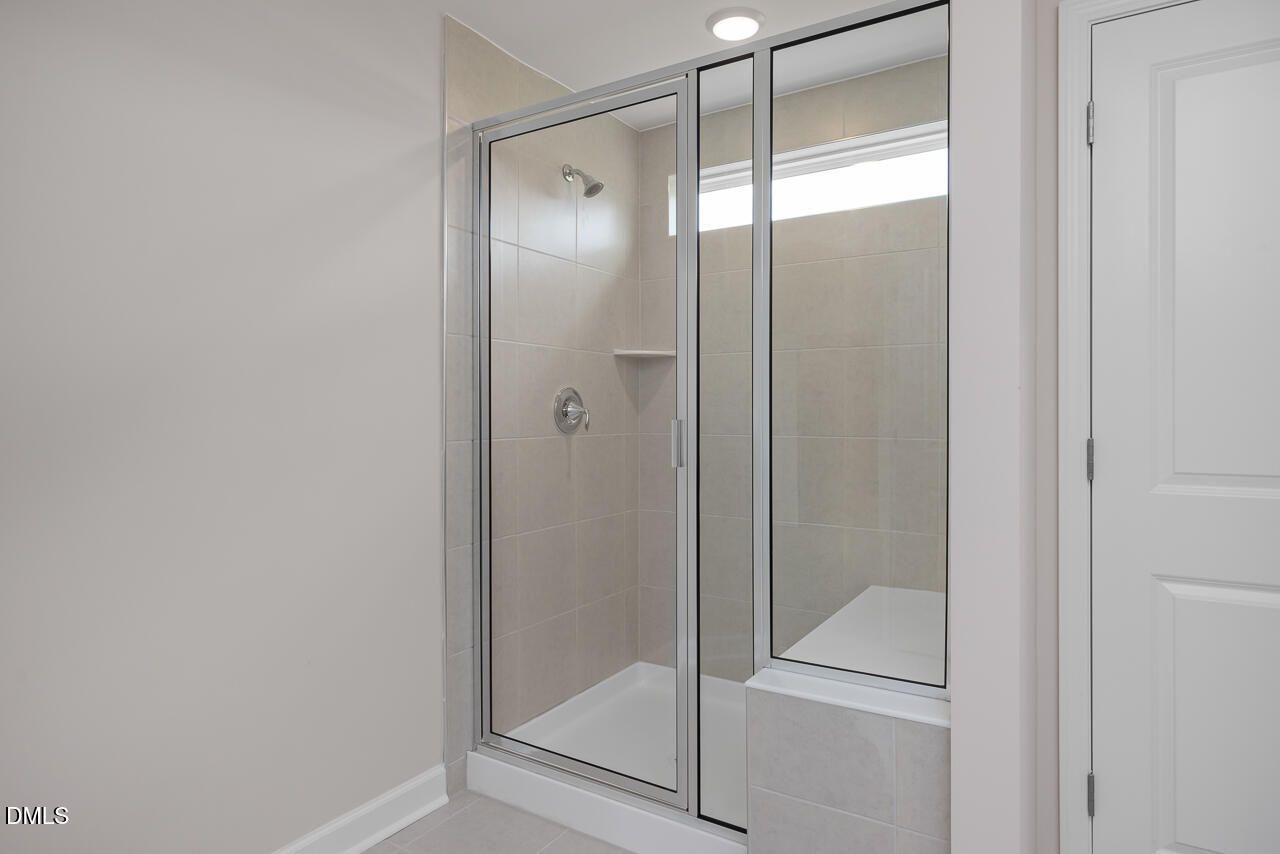 Modern glass-enclosed walk-in shower with neutral tile in a Davidson Homes Graham floor plan in Springvale, Fuquay-Varina.