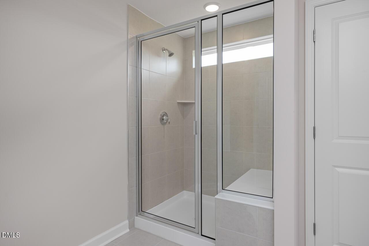 Modern glass-enclosed walk-in shower with neutral tile in a Davidson Homes Graham floor plan in Springvale, Fuquay-Varina.