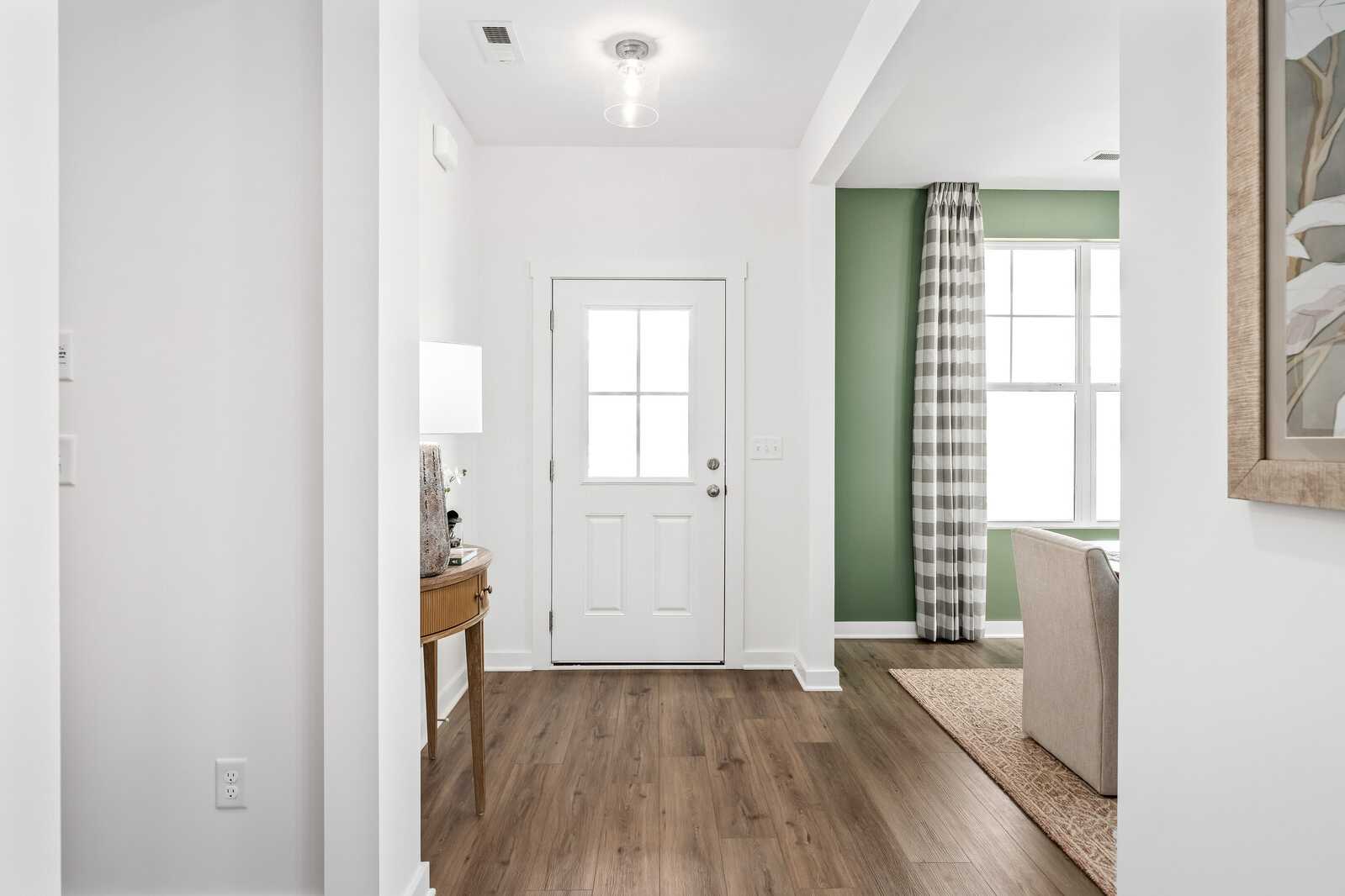 Spacious entryway at Calista Farms in White House TN with hardwood floors, white paneled door, and adjacent green-curtained room