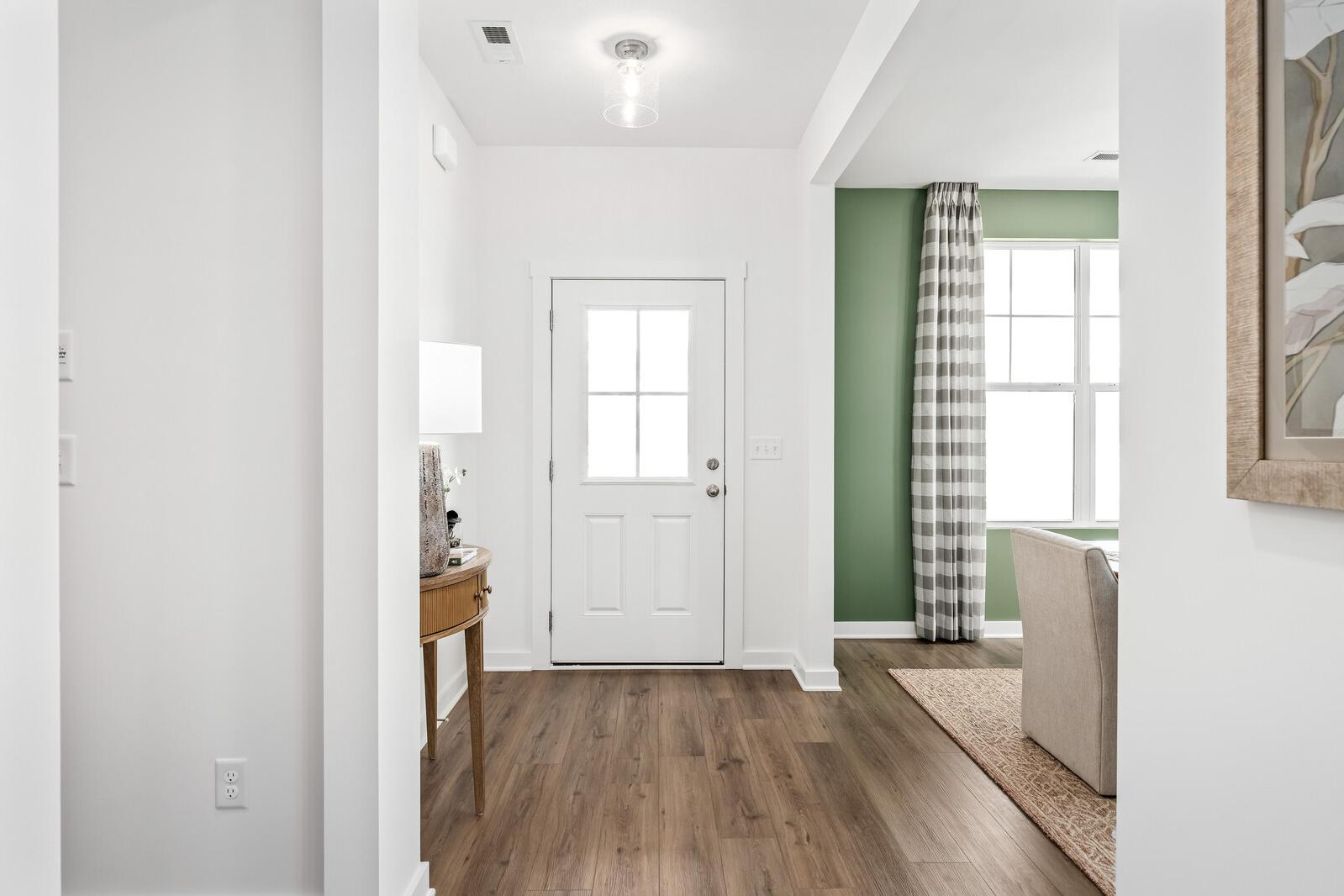 Spacious entryway at Calista Farms in White House TN with hardwood floors, white paneled door, and adjacent green-curtained room