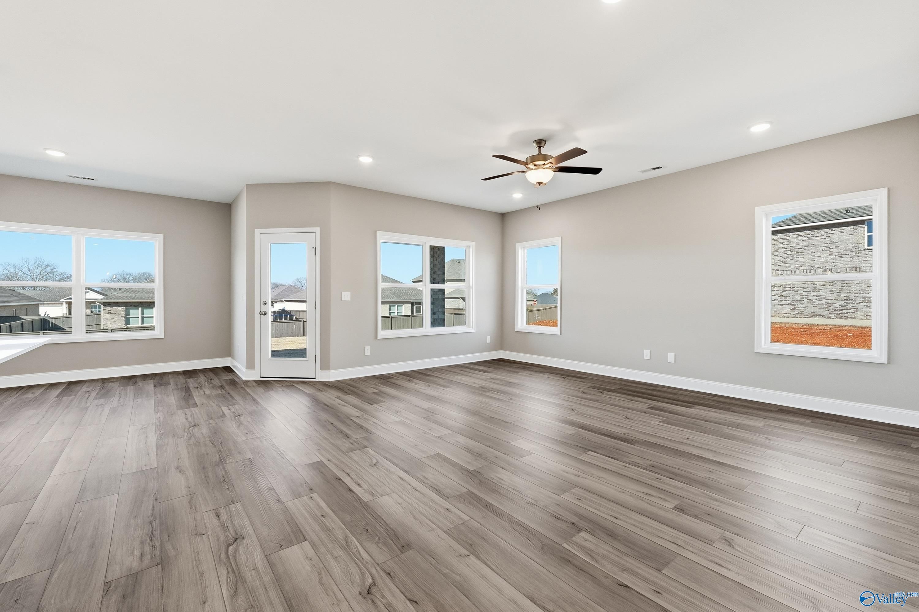 Spacious living room with gray hardwood floors, large windows, ceiling fan, and French doors to patio in Davidson Homes The Franklin C, New Market, AL
