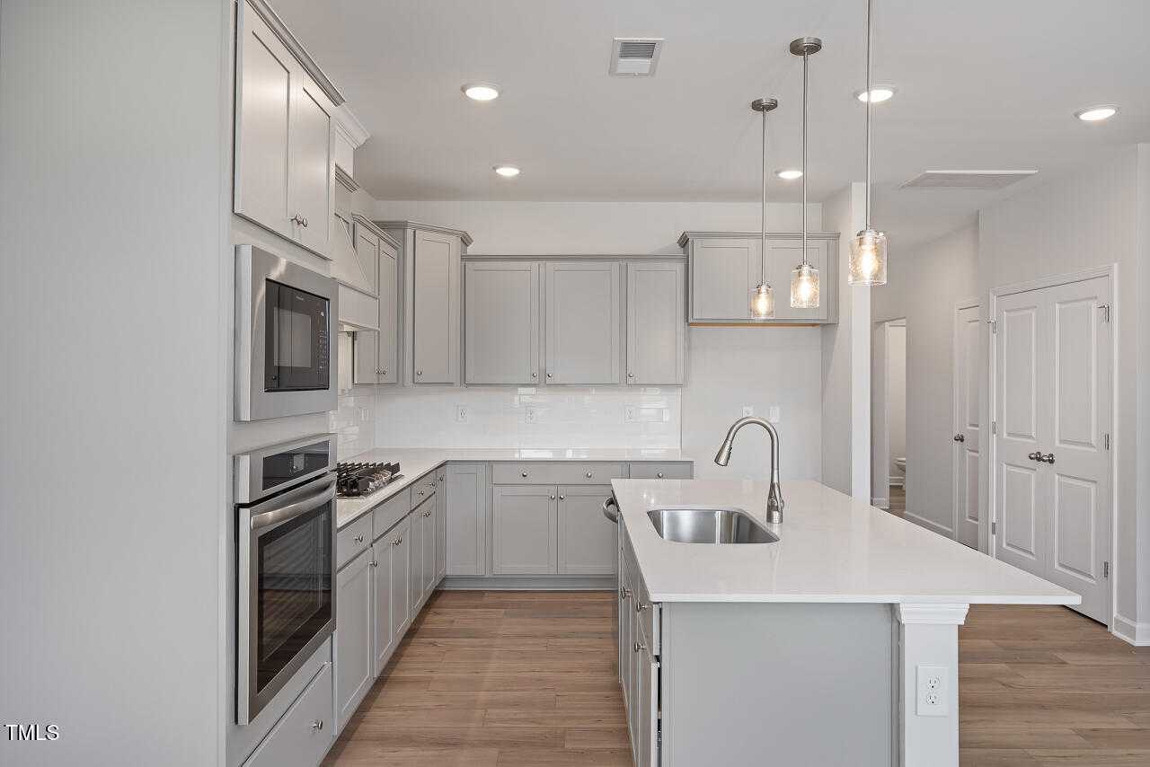 Modern gray kitchen with stainless appliances, white subway backsplash, and large island in Davidson Homes The Graham, Fuquay-Varina, NC