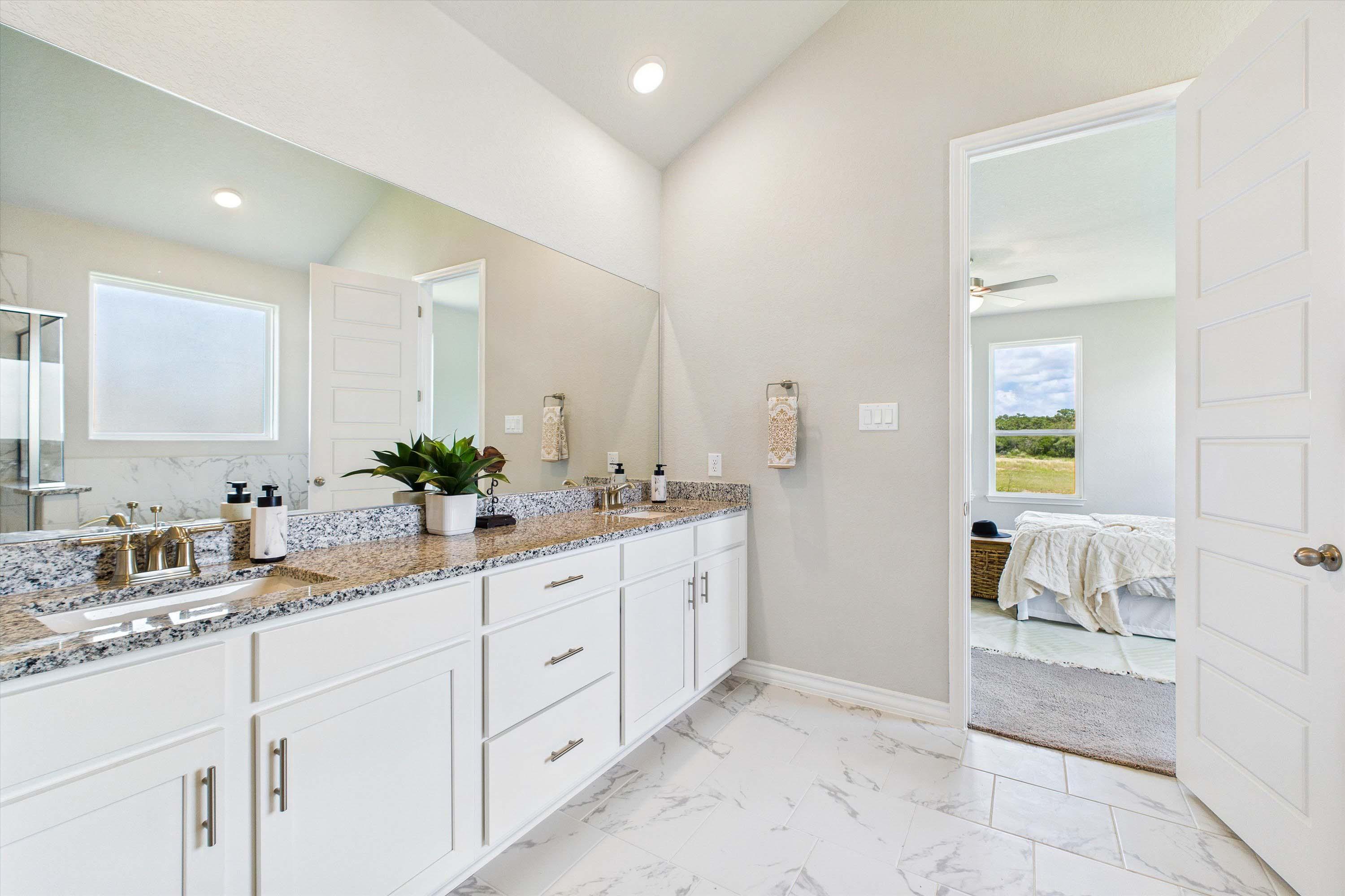 Spacious master bathroom in The Foster featuring double vanities, granite countertops, and elegant tile flooring.
